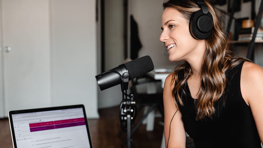 A woman wearing headphones leans in to a Shure SM7 microphone.