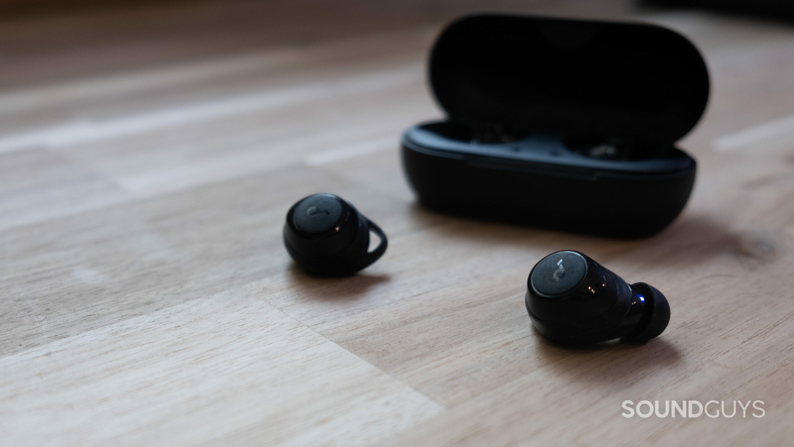 The Anker Soundcore Life A1 earbuds next to their case sit on a wood surface.