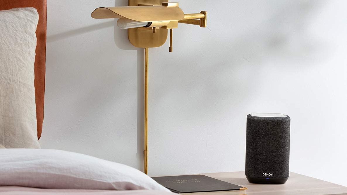 The Denon Home 150 speaker standing on a bedside table.