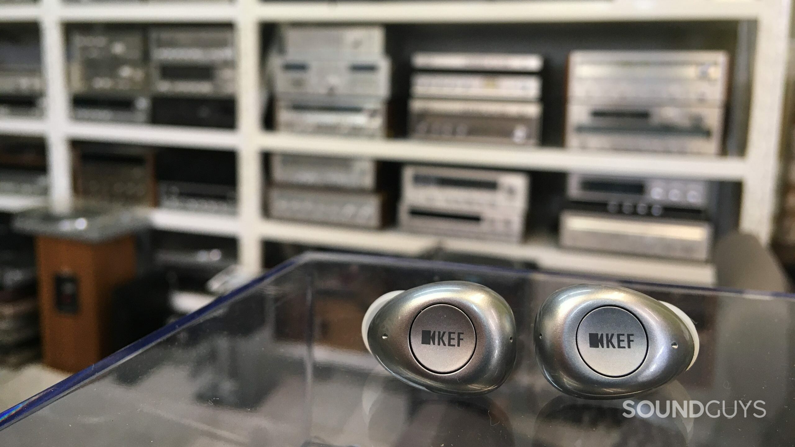The KEF Mu3 earbuds contrasted with some vintage stereo equipment.