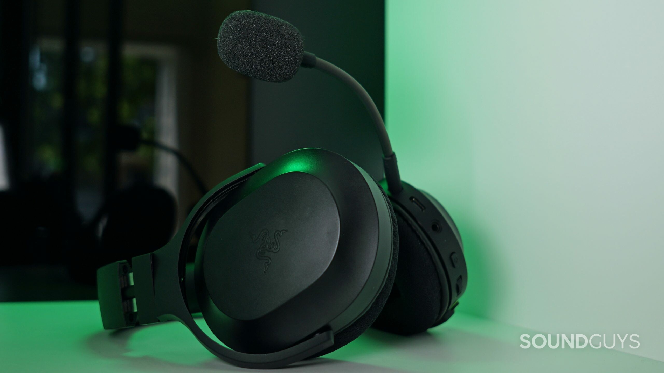 The Razer Barracuda X lays on a white shelf in front of a black reflective surface with a green light shining down.
