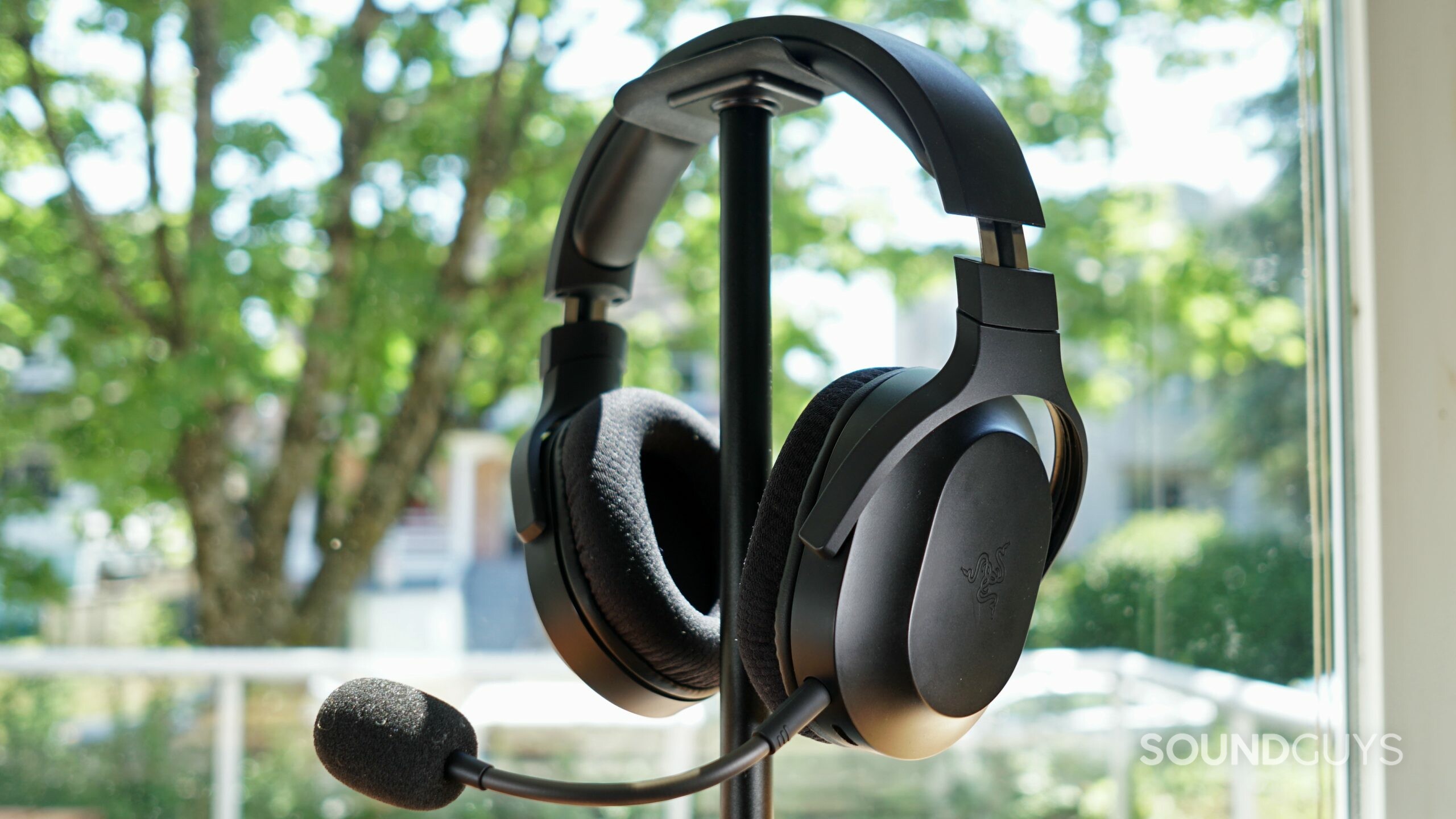 The Razer Barracuda X sits on a headphone stand in front of a window