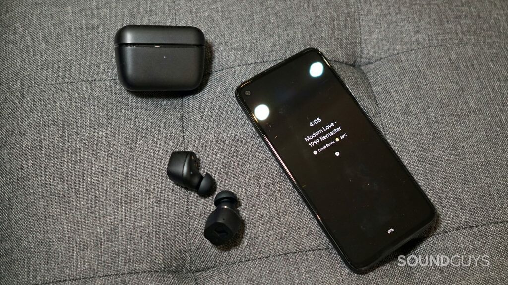 The Sennheiser CX True Wireless lays on a fabric surface next to its charging case and a Google Pixel 4a.