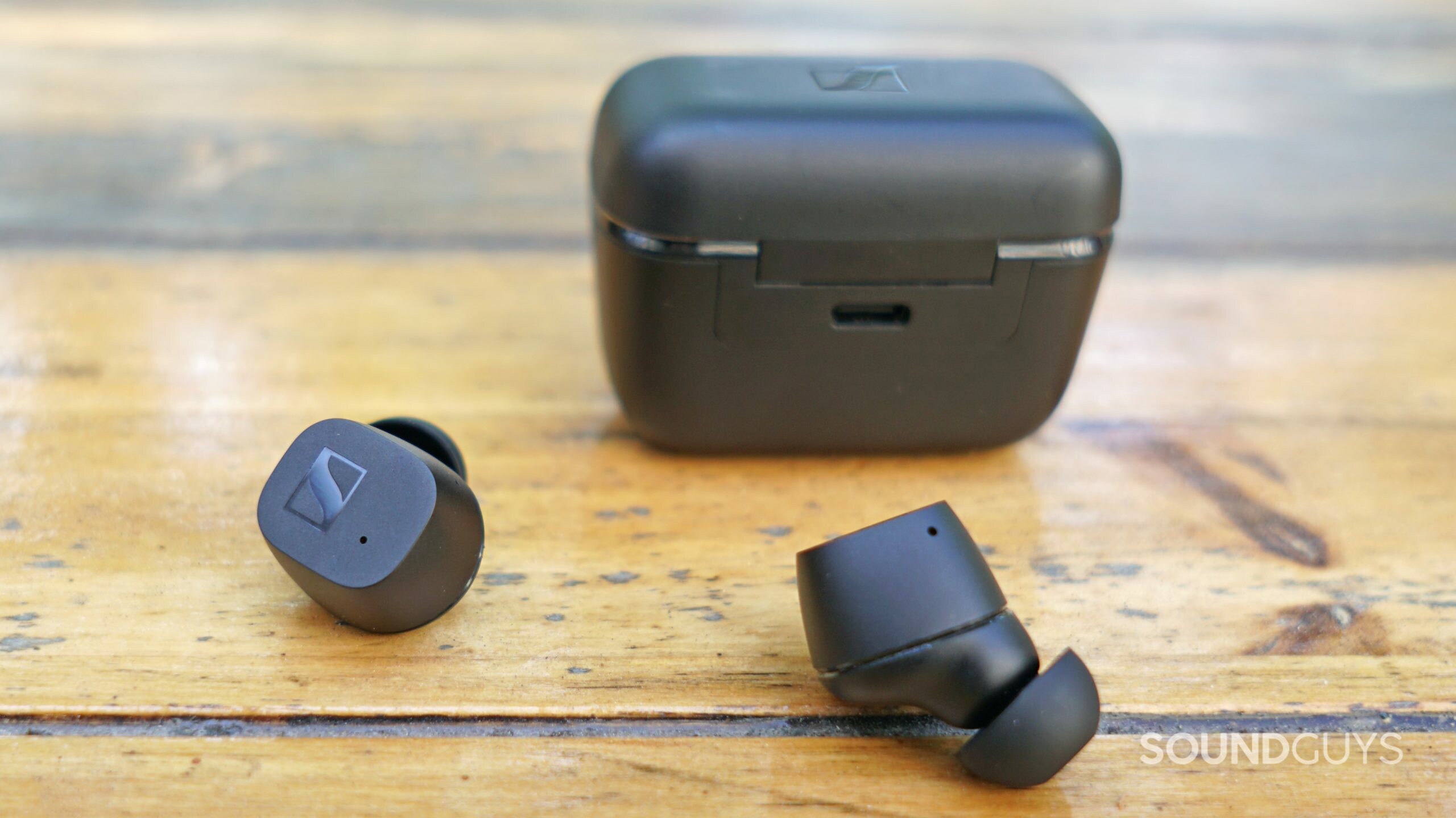 The Sennheiser CX True Wireless earbuds lay in front of its charging case, with its charging case in view.