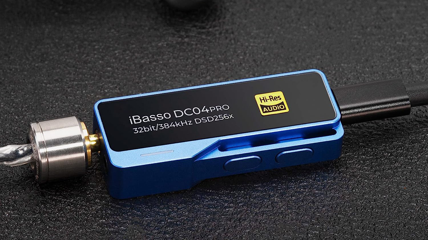 A manufacturer photo of the iBasso DC04Pro sitting atop a black surface, with USB cable and 3.5mm cables inserted.
