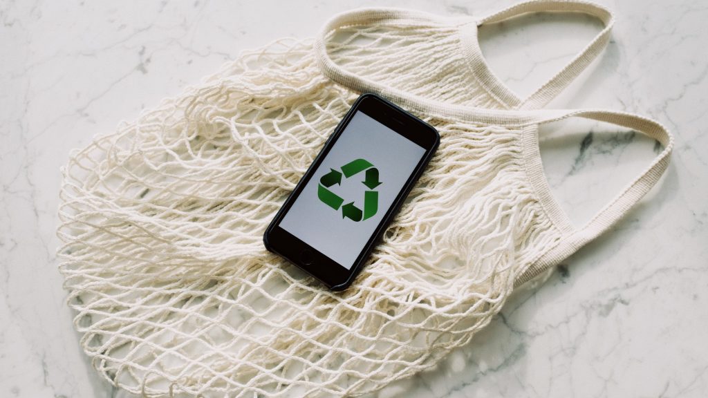Mobile phone with green recycling sign and mesh bag.