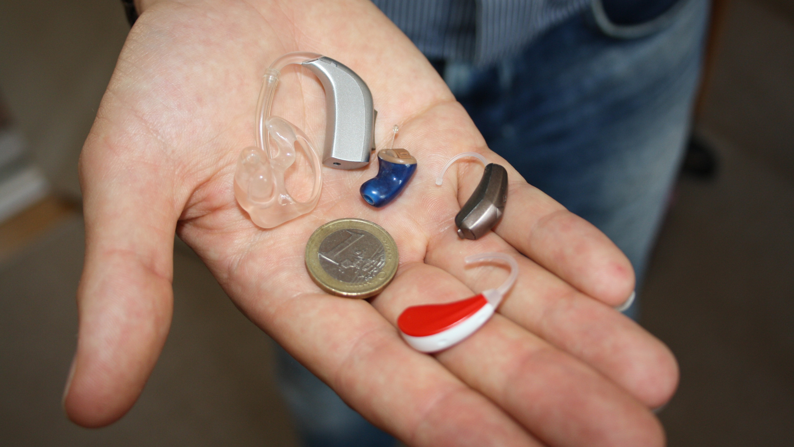 Man holding a selection of hearing aids and a one Euro coin.