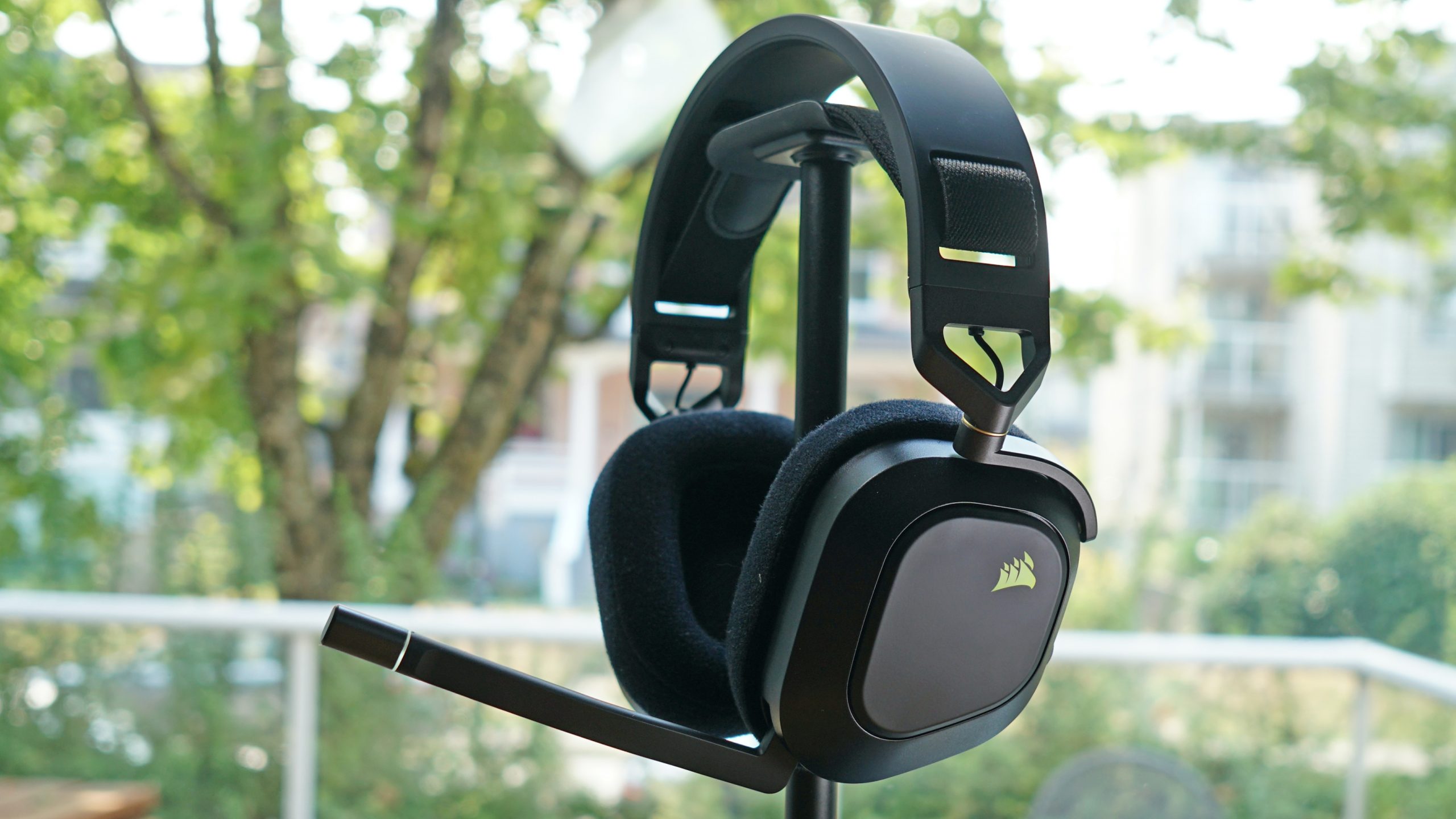 The Corsair HS80 RGB Wireless sits on a headphone stand in front of a window