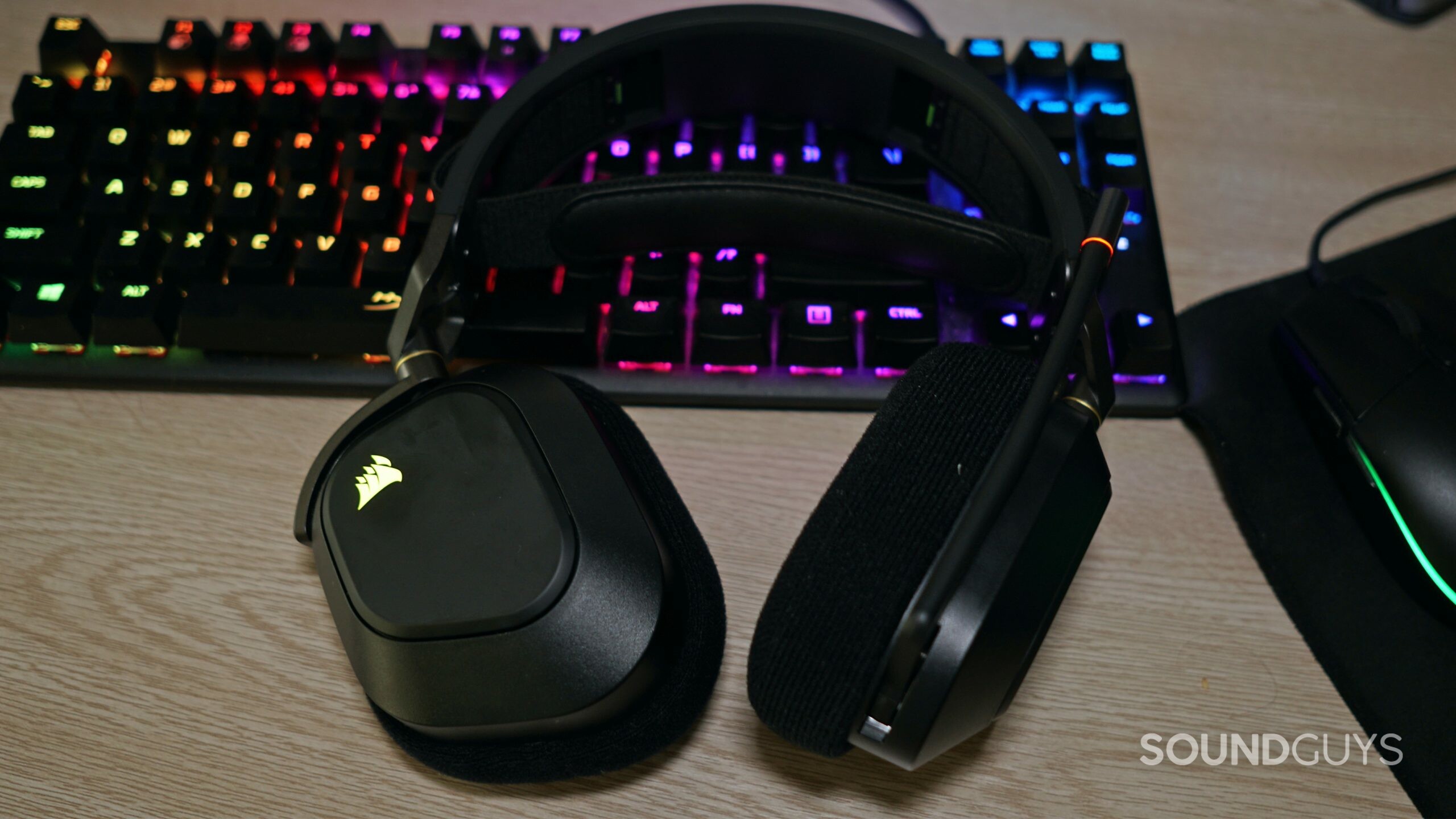 The Corsair HS80 RGB Wireless lays on a desk on top of a HyperX mechanical gaming keyboard, next to a Logitech gaming mouse