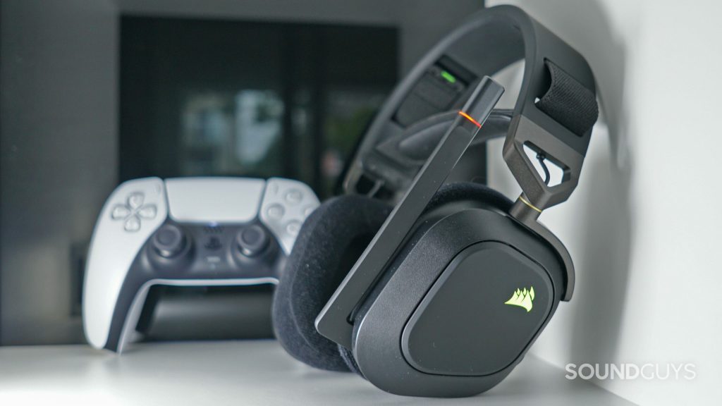 The Corsair HS80 RGB Wireless sits on a white shelf, with a PlayStation DualSense controller in the background.