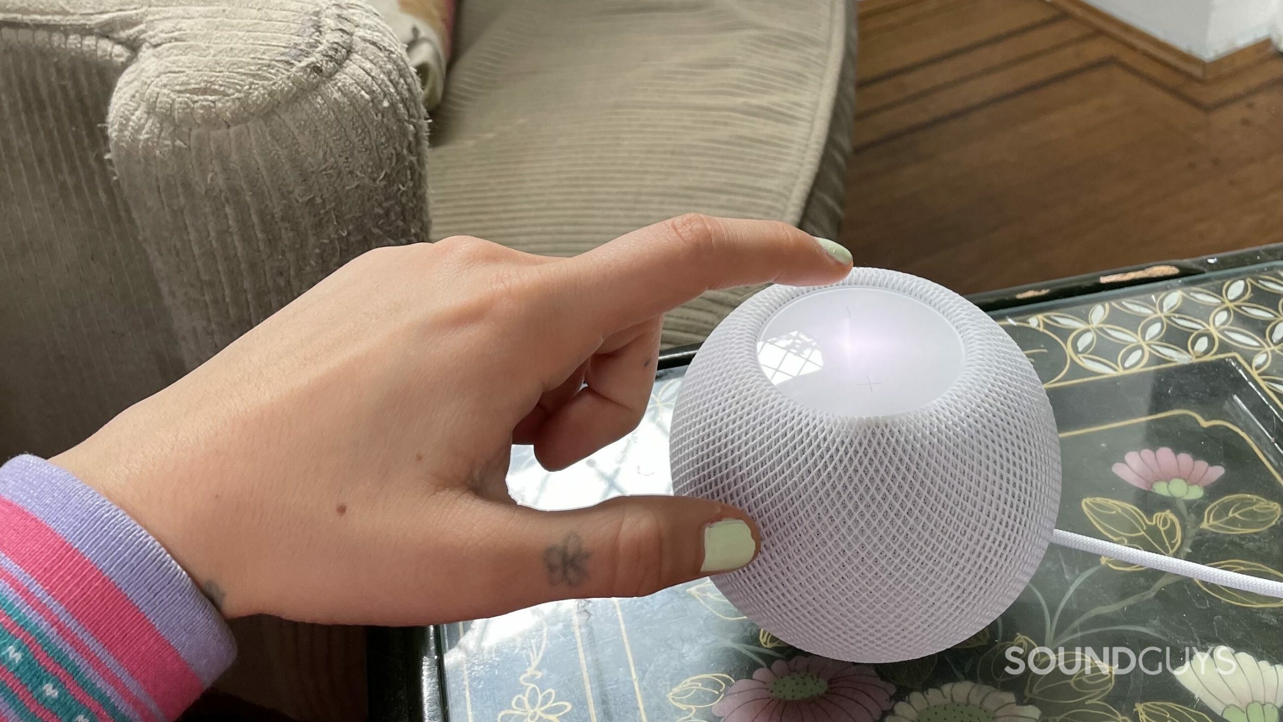 Womans hand about to tap the touchpad of the Apple HomePod mini.