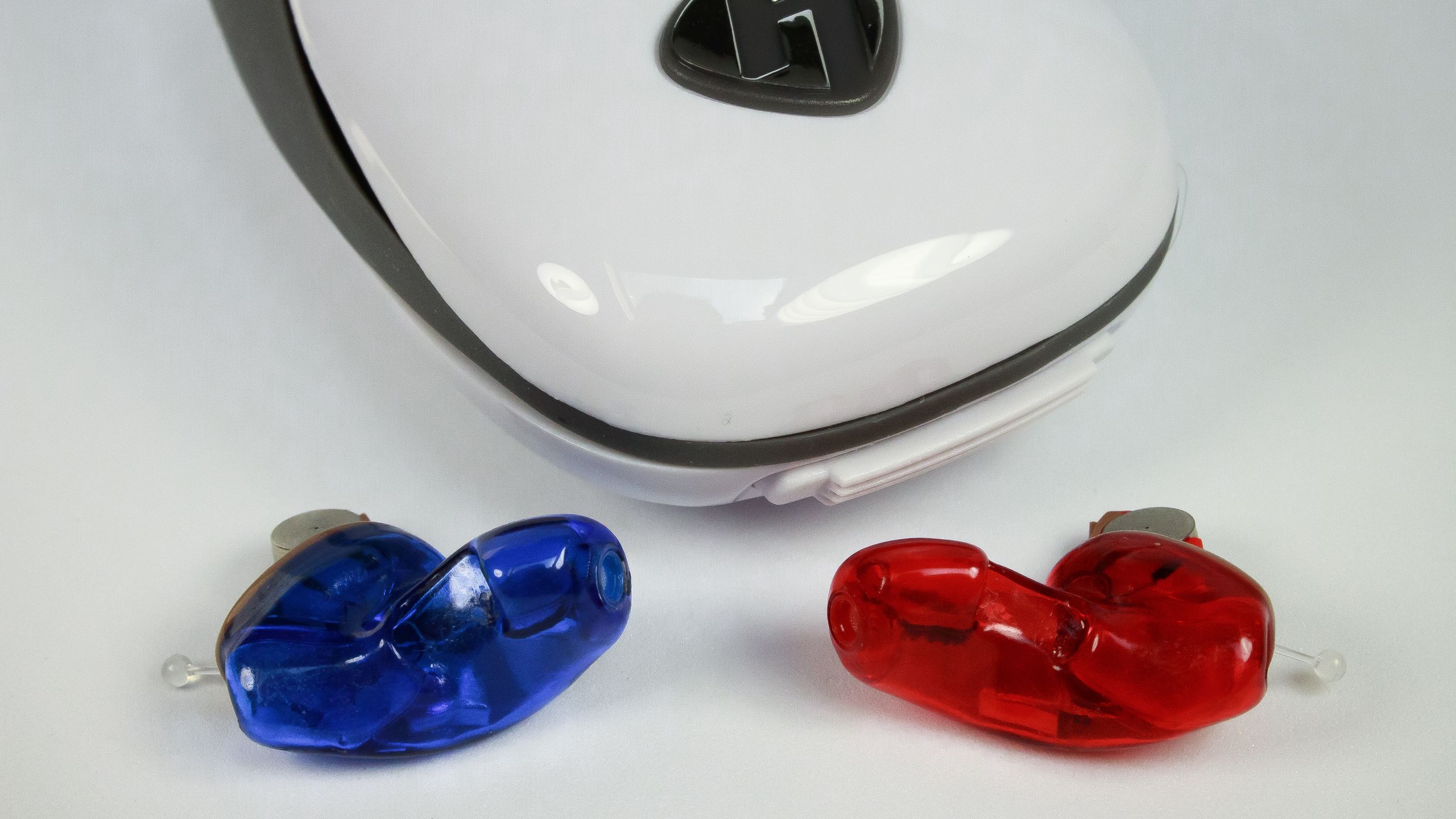 A pair of ITC hearing aids with exposed battery, laying next to a white case.