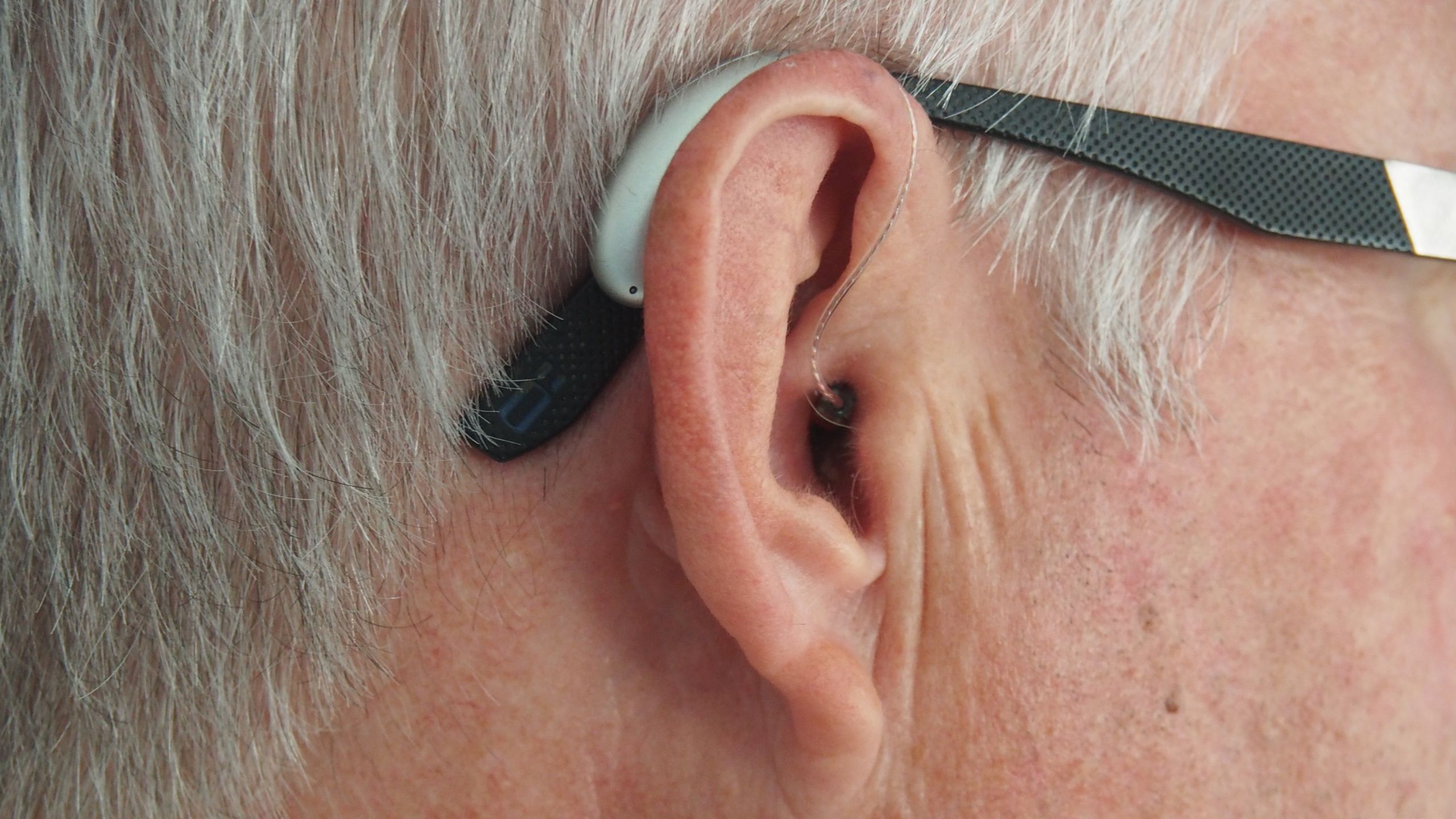 Man Wearing RIC Hearing Aid in Right Ear A man with glasses wearing a RIC hearing aid on his right ear.