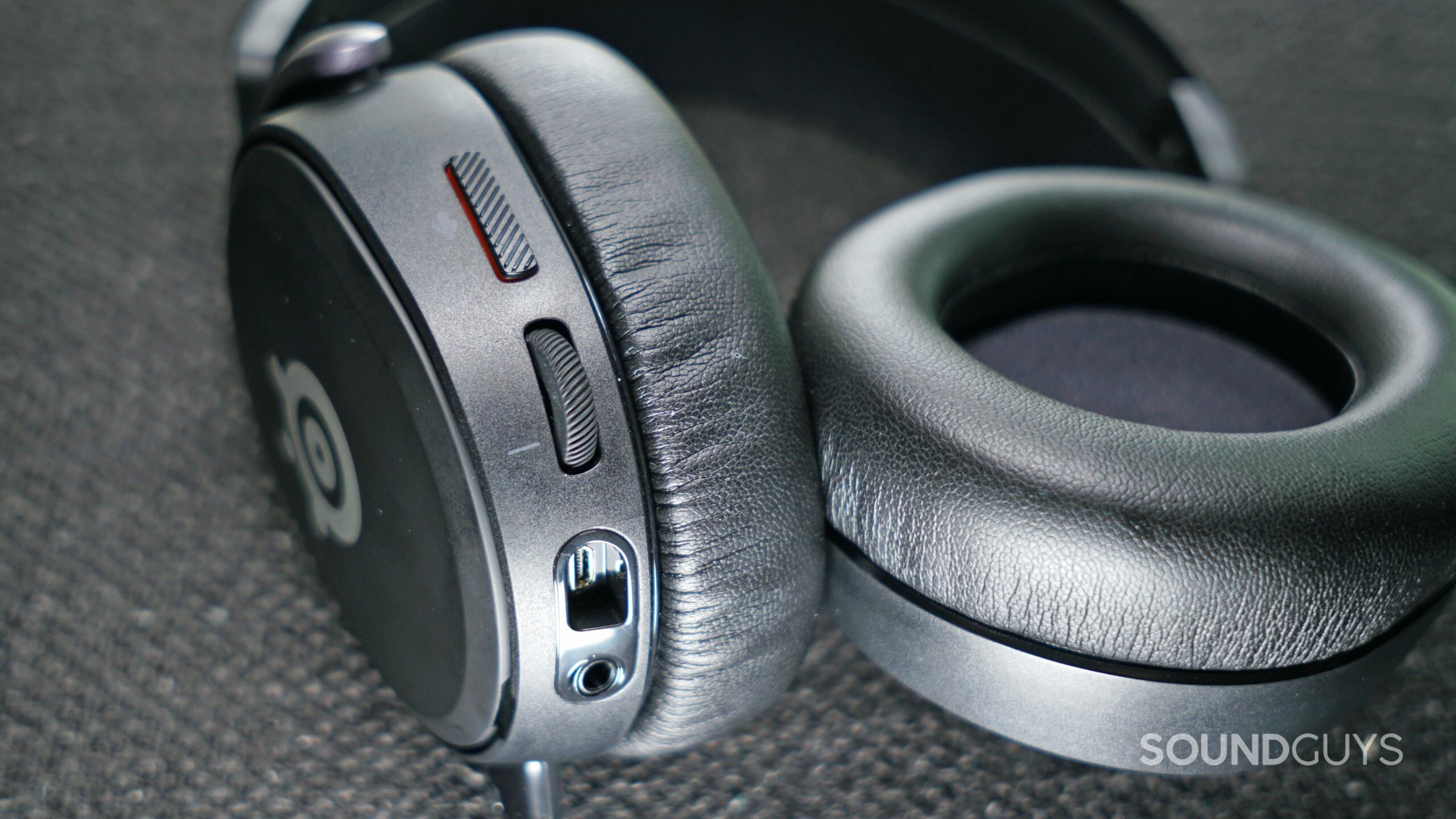The SteelSeries Arctis Prime lays on a fabric surface with its on-ear controls in view.