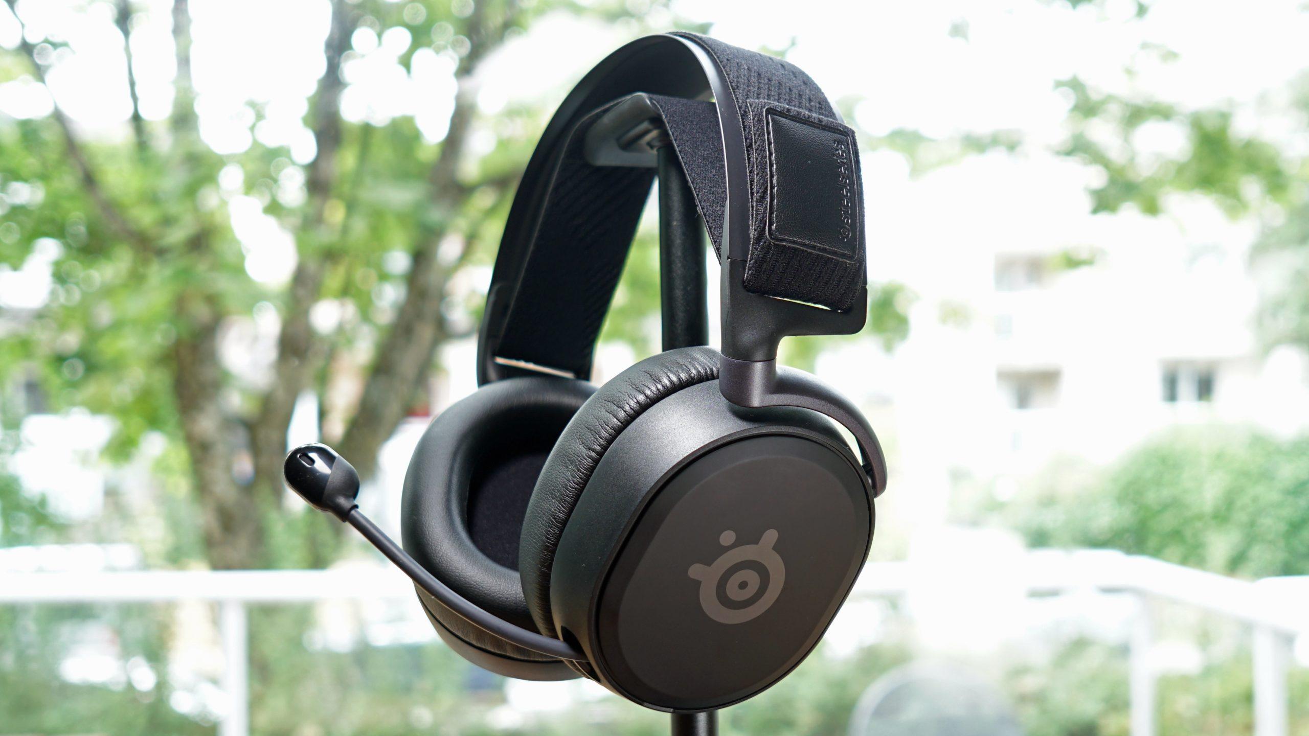 The SteelSeries Arctis Prime gaming headset sits on headphone stand in front of a window.