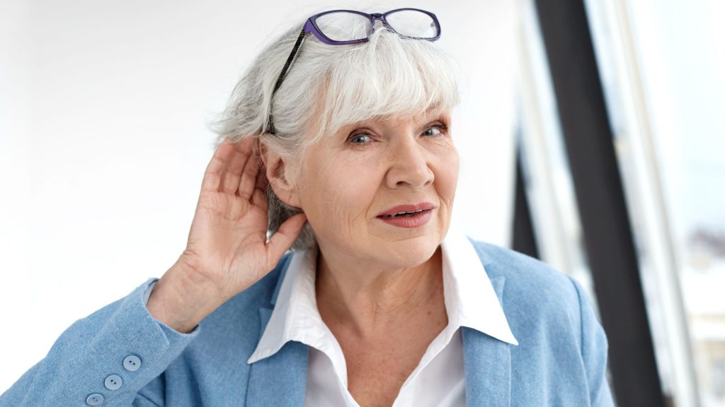 Elderly woman putting a hand behind her ear to hear better.
