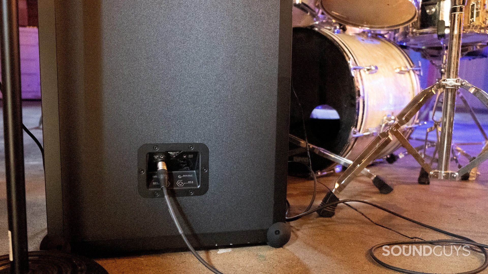 Back of SoundBoks Gen. 3) with an XLR cable plugged in and a drum kit in the background.