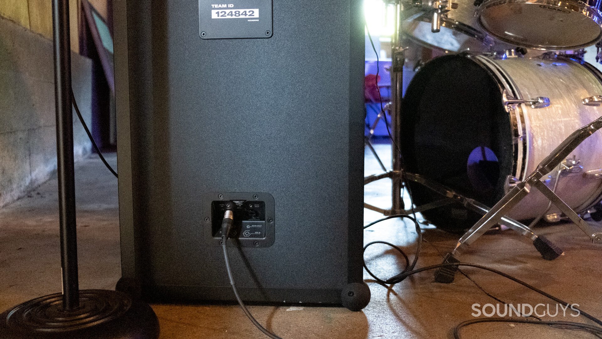 Back of SoundBoks (Gen. 3) with an XLR cable plugged in. A drum kit and microphone stand are visible.