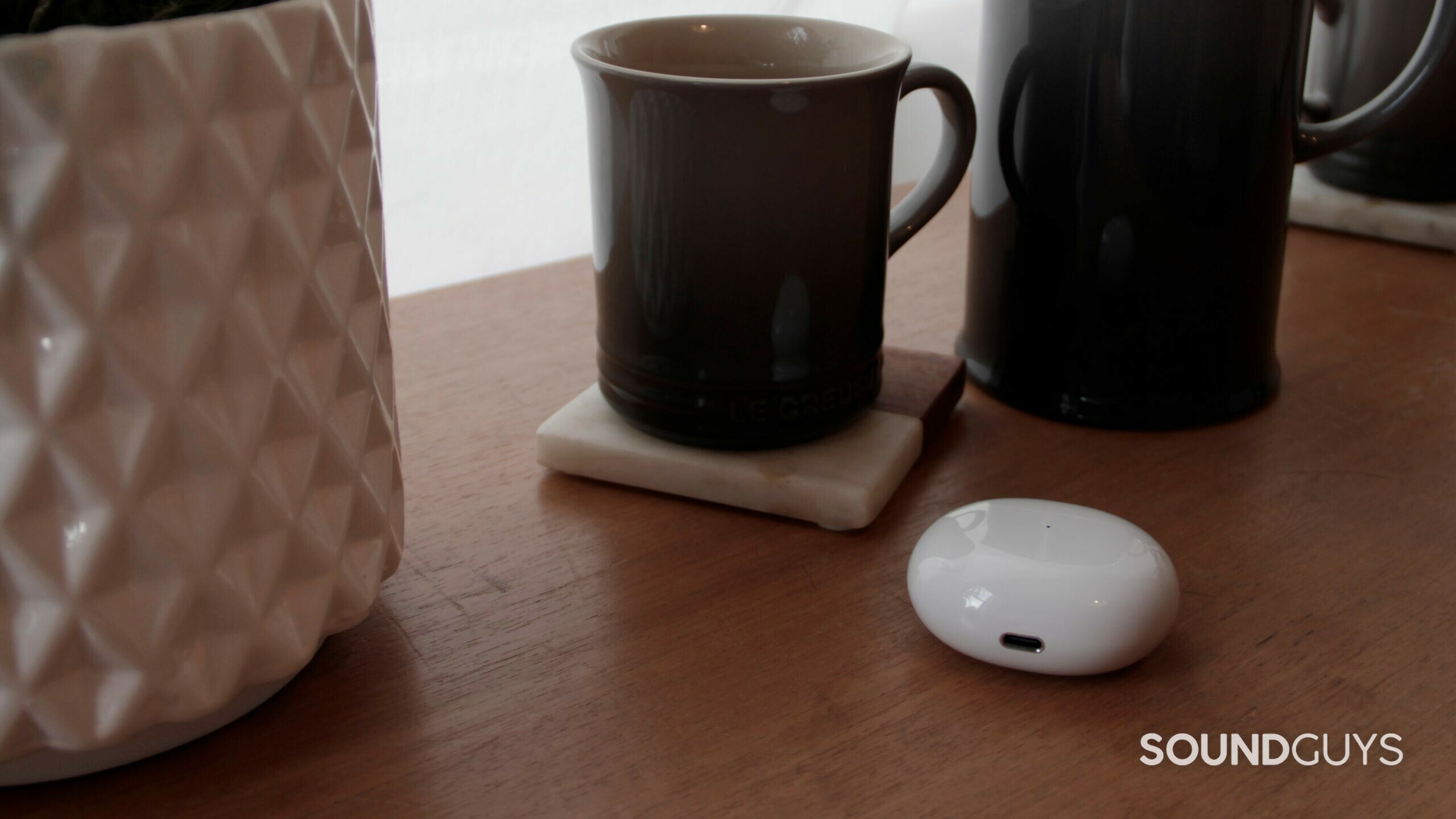 Closed case of TCL MOVEAUDIO S600 on a wood table with a coffee mug and plant pot.