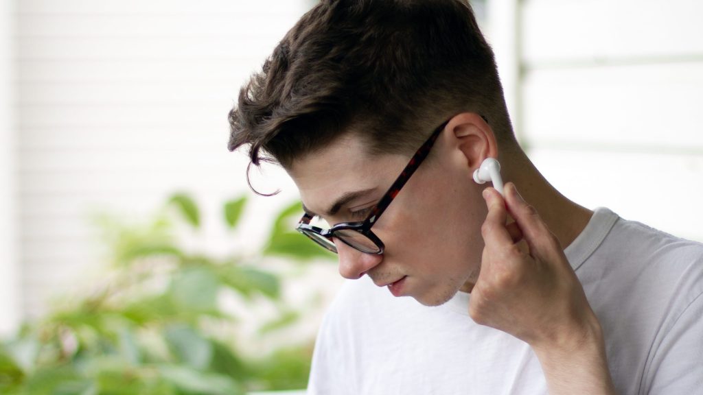 Man looks down putting TCL MOVEAUDIO S600 earbud into his left ear.