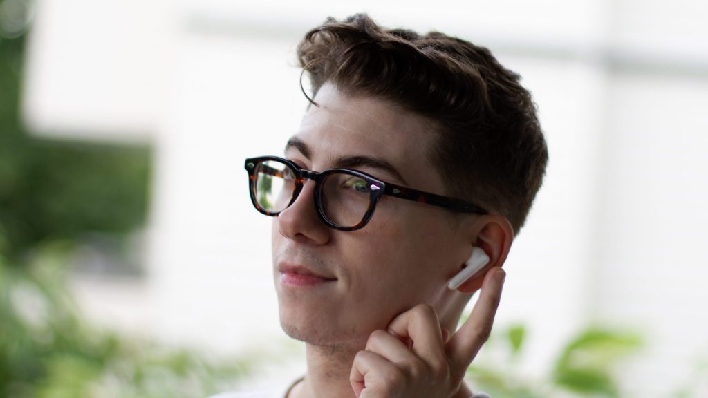 A three quarter angle of a man's face while he uses the touch control of the TCL MOVEAUDIO S600 earphone.