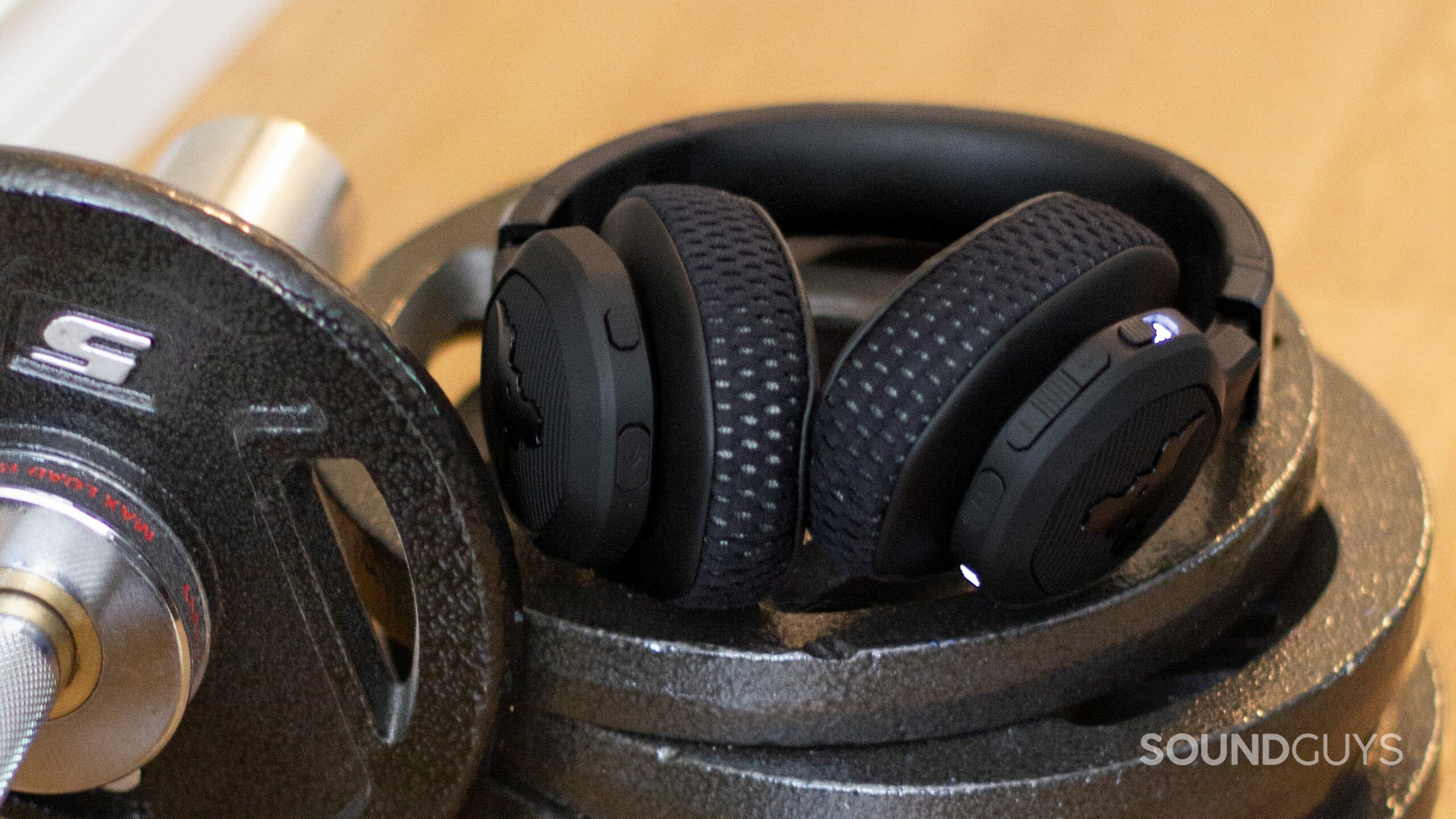 Under Armour Project Rock by JBL headphones rest on a dumb bell weight plate stack on the floor beside a dumb bell.