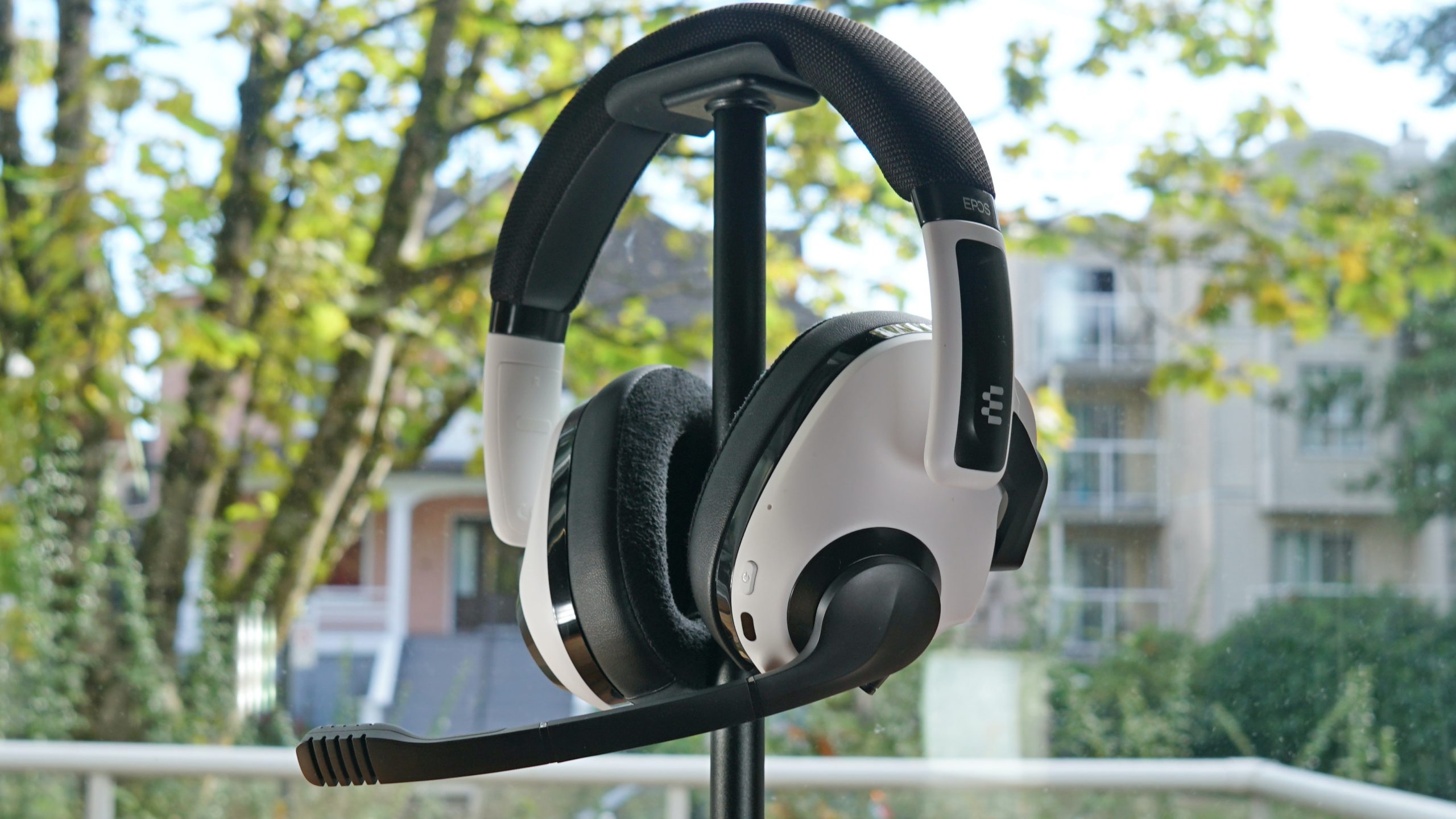The EPOS H3 Hybrid sits on a headphone stand in front of a window.