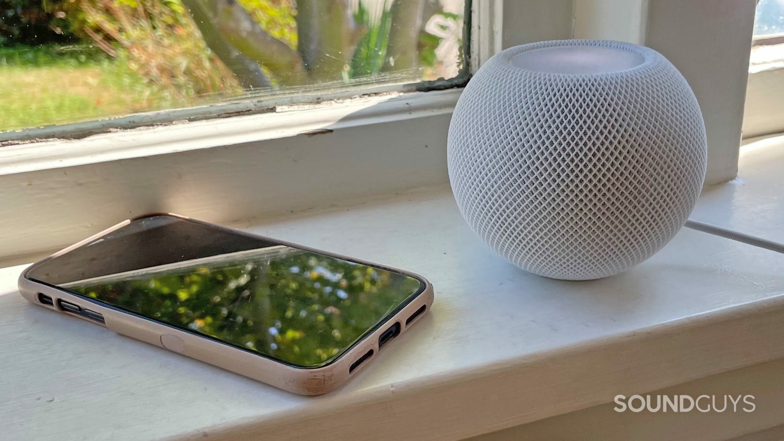 An iPhone and Apple HomePod mini sitting on a windowsill.