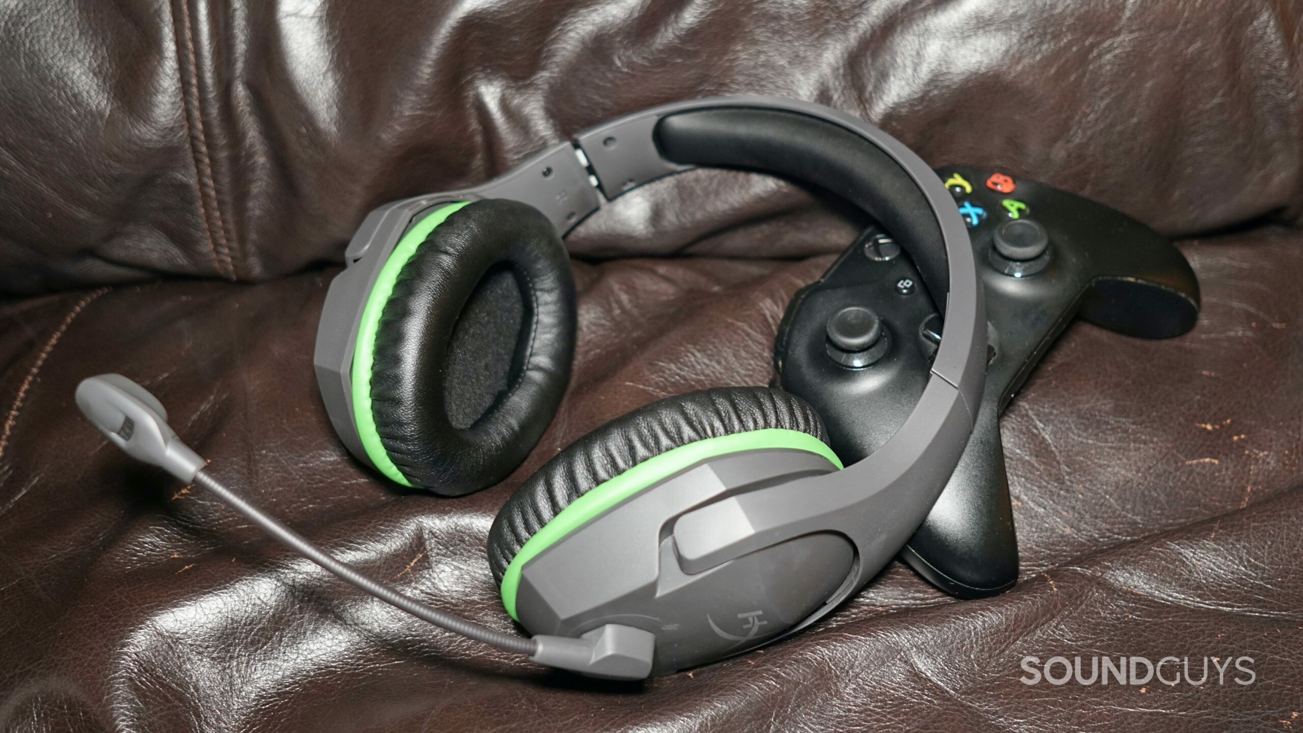 The HyperX CloudX Stinger Core lays on a leather couch, next to an Xbox One controller.