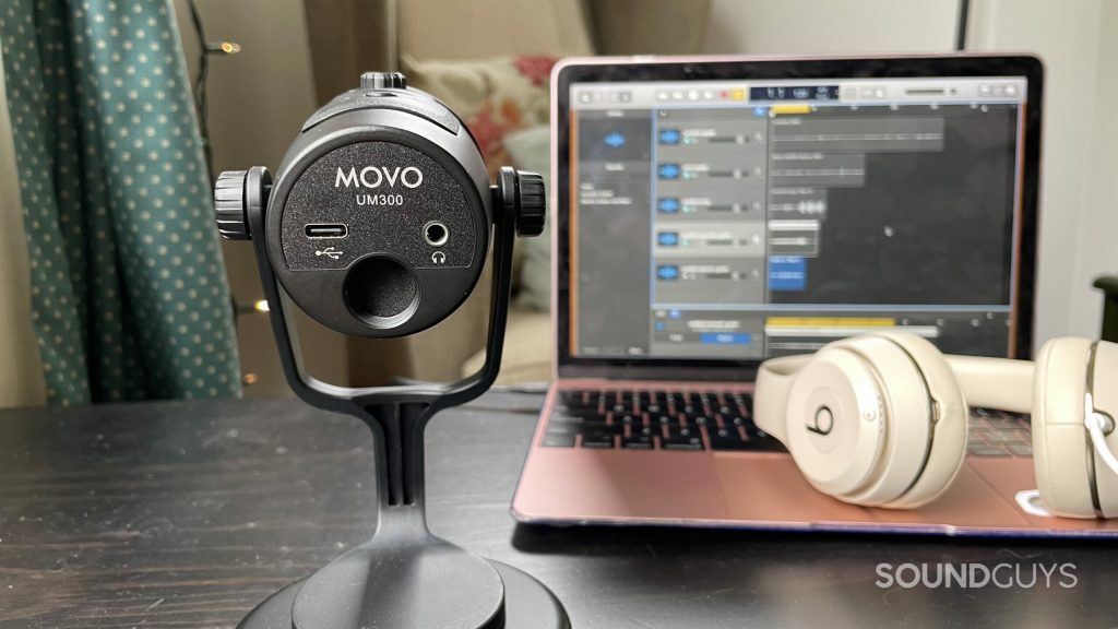 Underside of the Movo UM300 showing the ports and threaded mount. Beats headphones and a laptop with Garageband open are visible in the background.