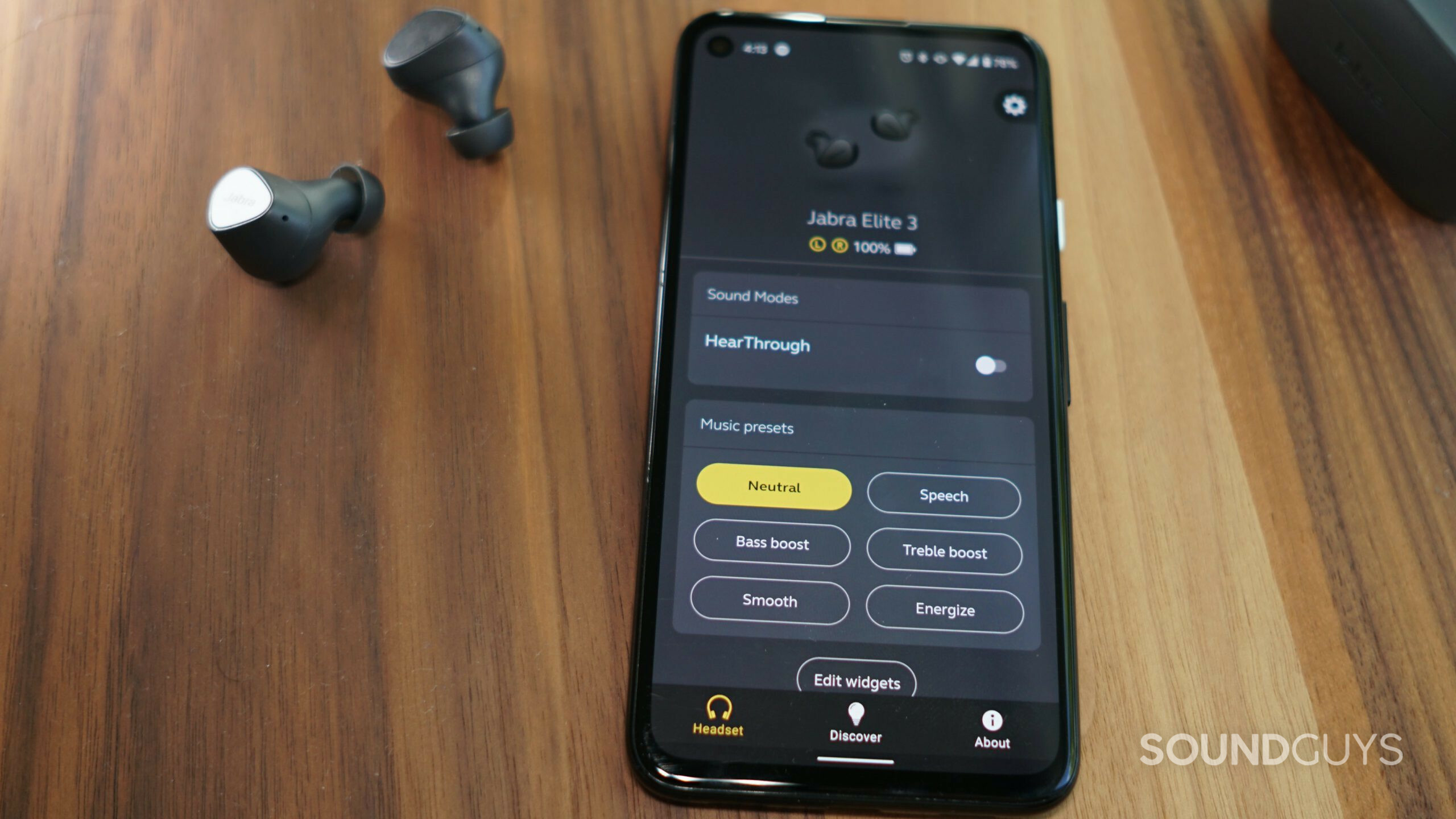 The Jabra Elite 3 true wireless earbuds lay on a wooden table next to a Google Pixel 4a with the Jabra Sound + app open.