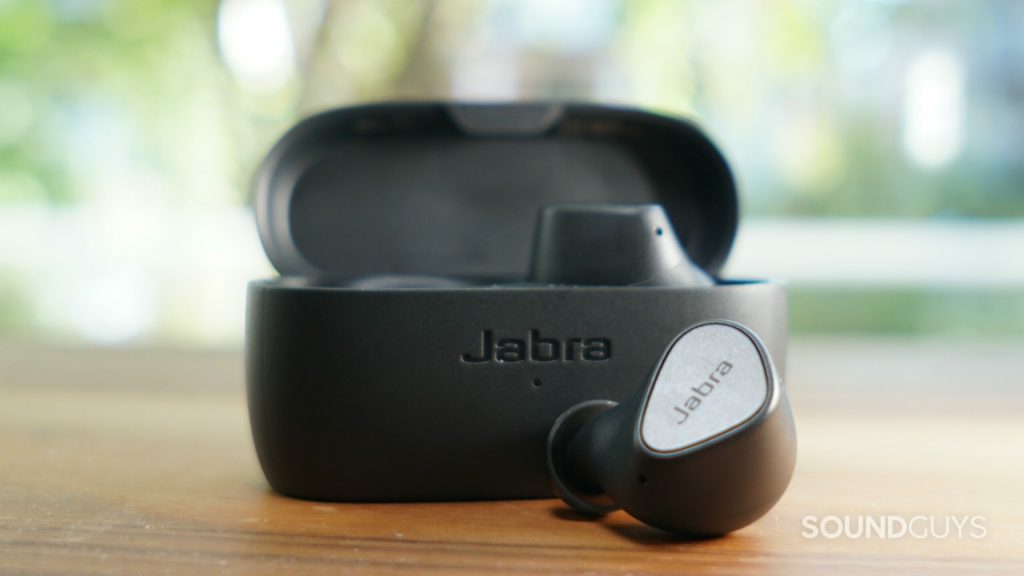 The Jabra Elite 3 sits on a wooden table in front of a window with one bud out.