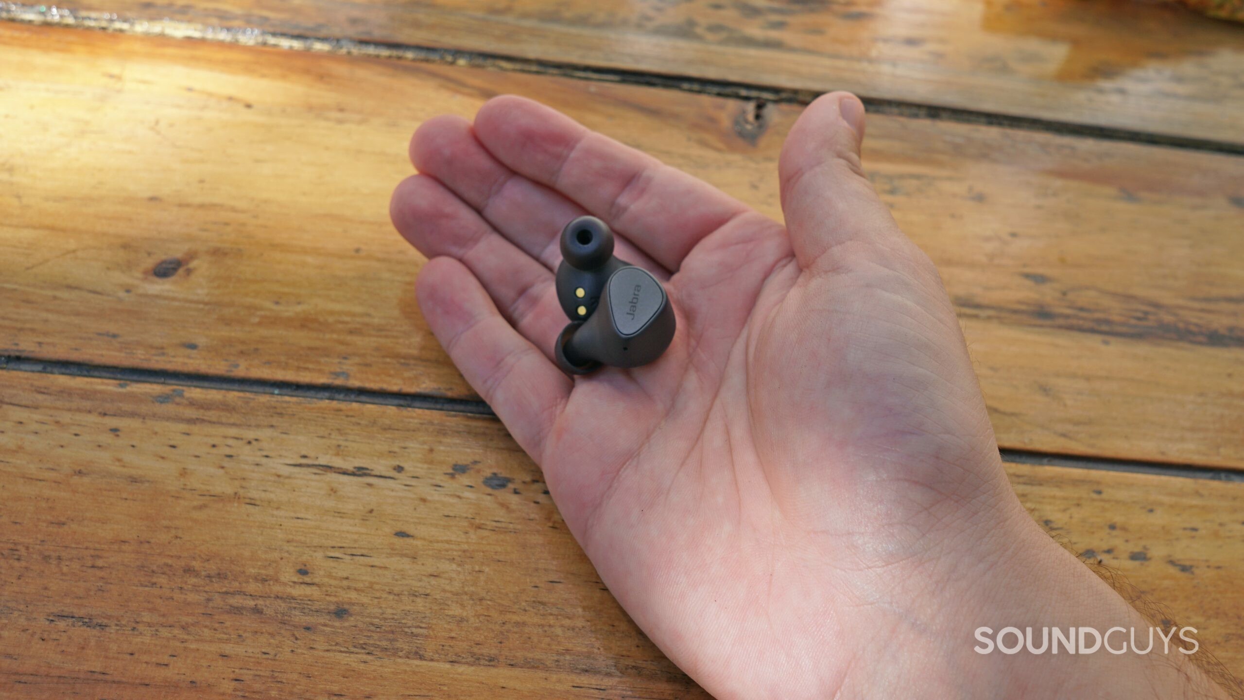 A hand holds the Jabra Elite 3 earbuds outisde