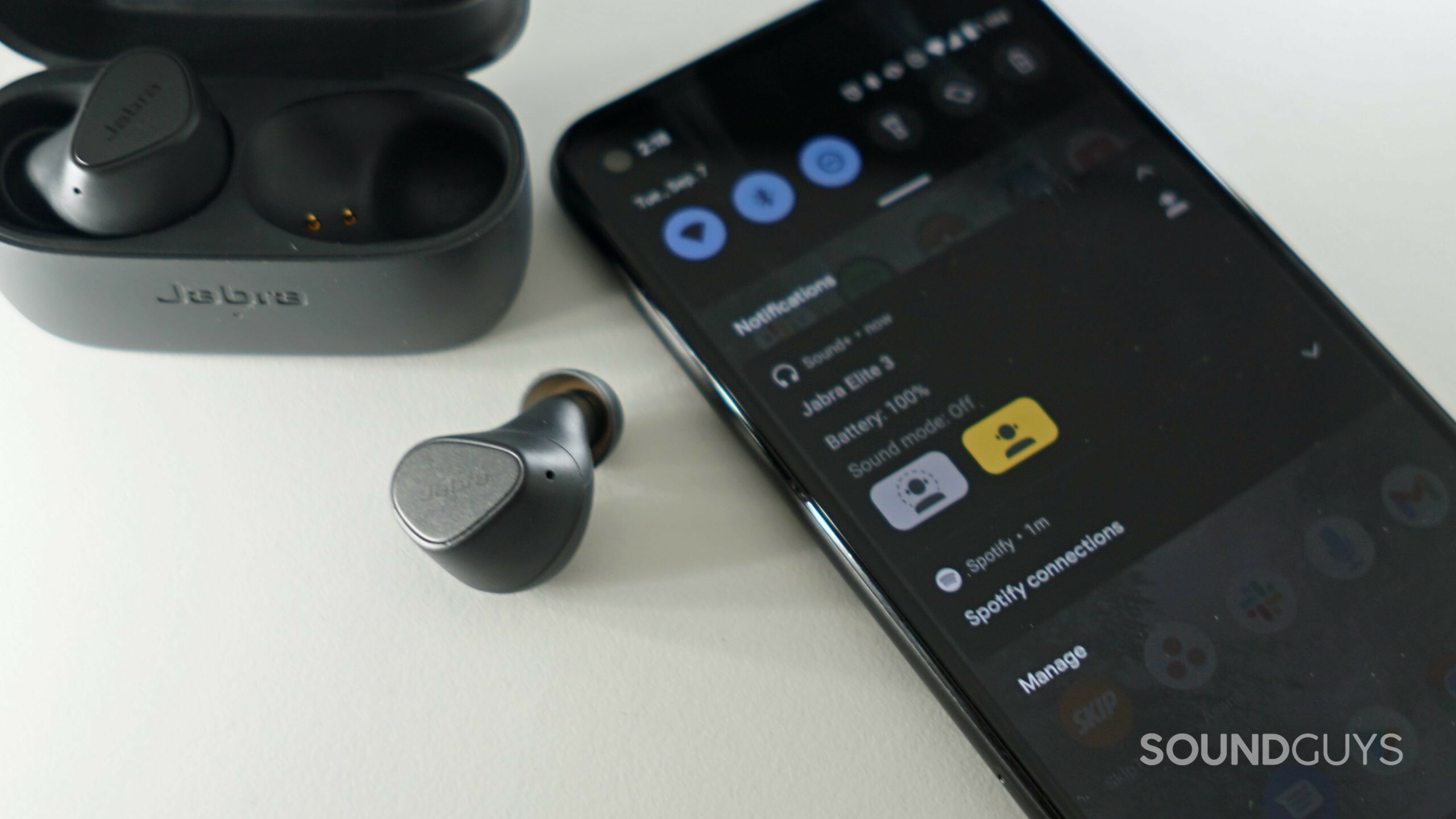 The Jabra Elite 3 lays on a white shelf next to a Google Pixel 4a with the quick control dropdown menu open.