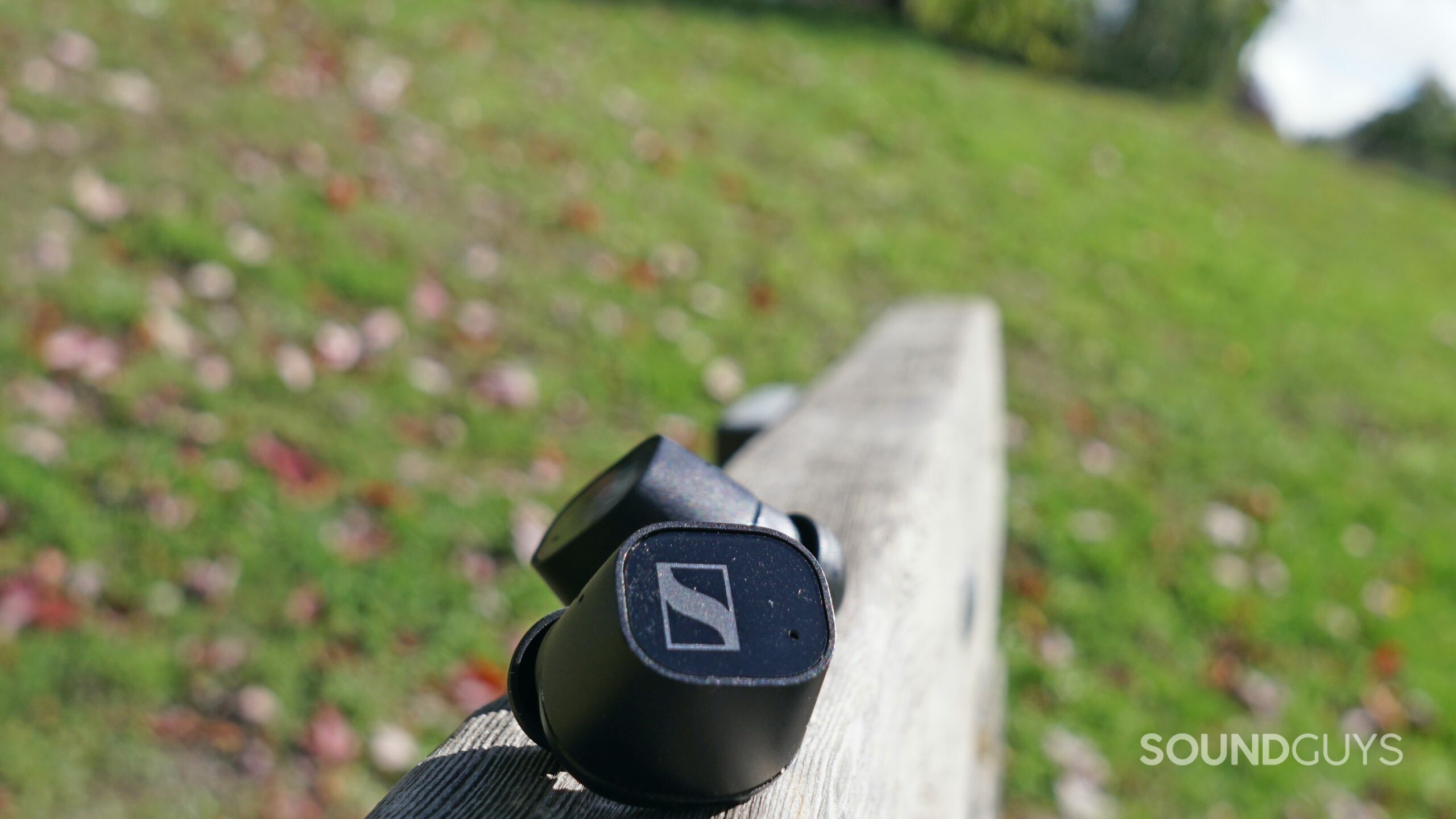 The Sennheiser CX Plus True Wireless earbuds lay on a wooden bench outside.