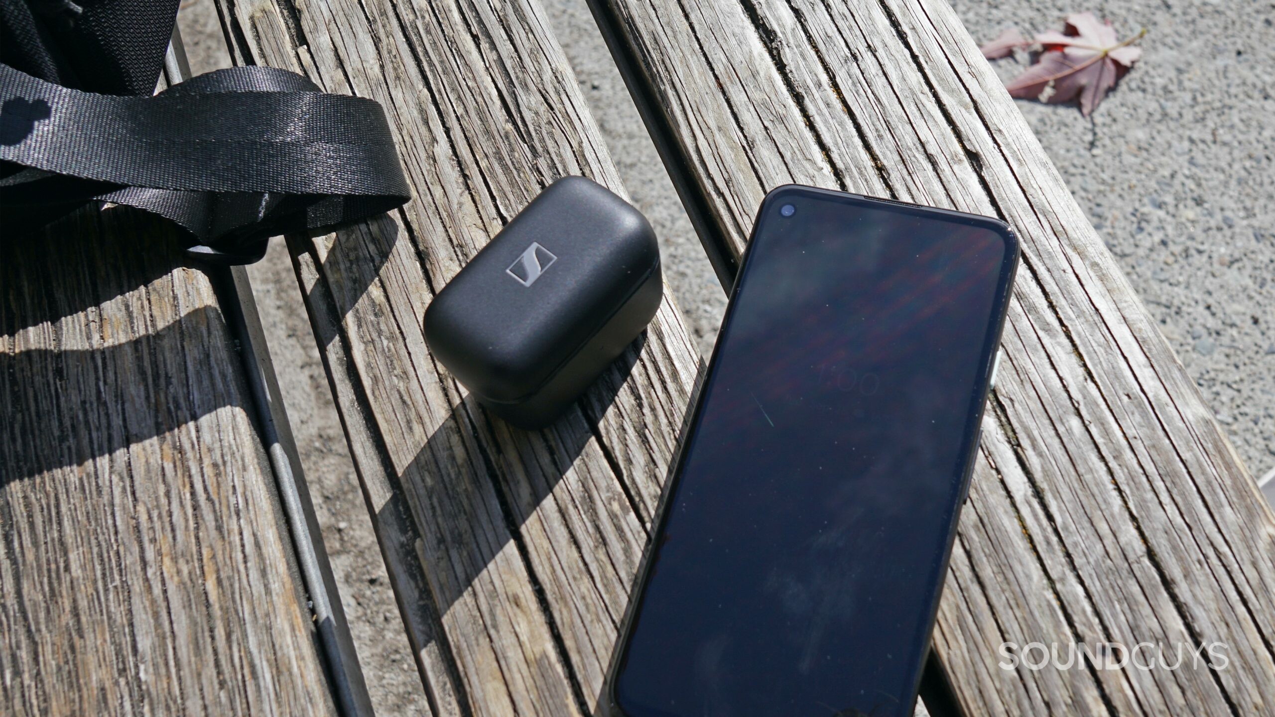 The Sennheiser CX Plus True Wireless earbuds case sits on a bench next to a camera bag and a Google Pixel 4a