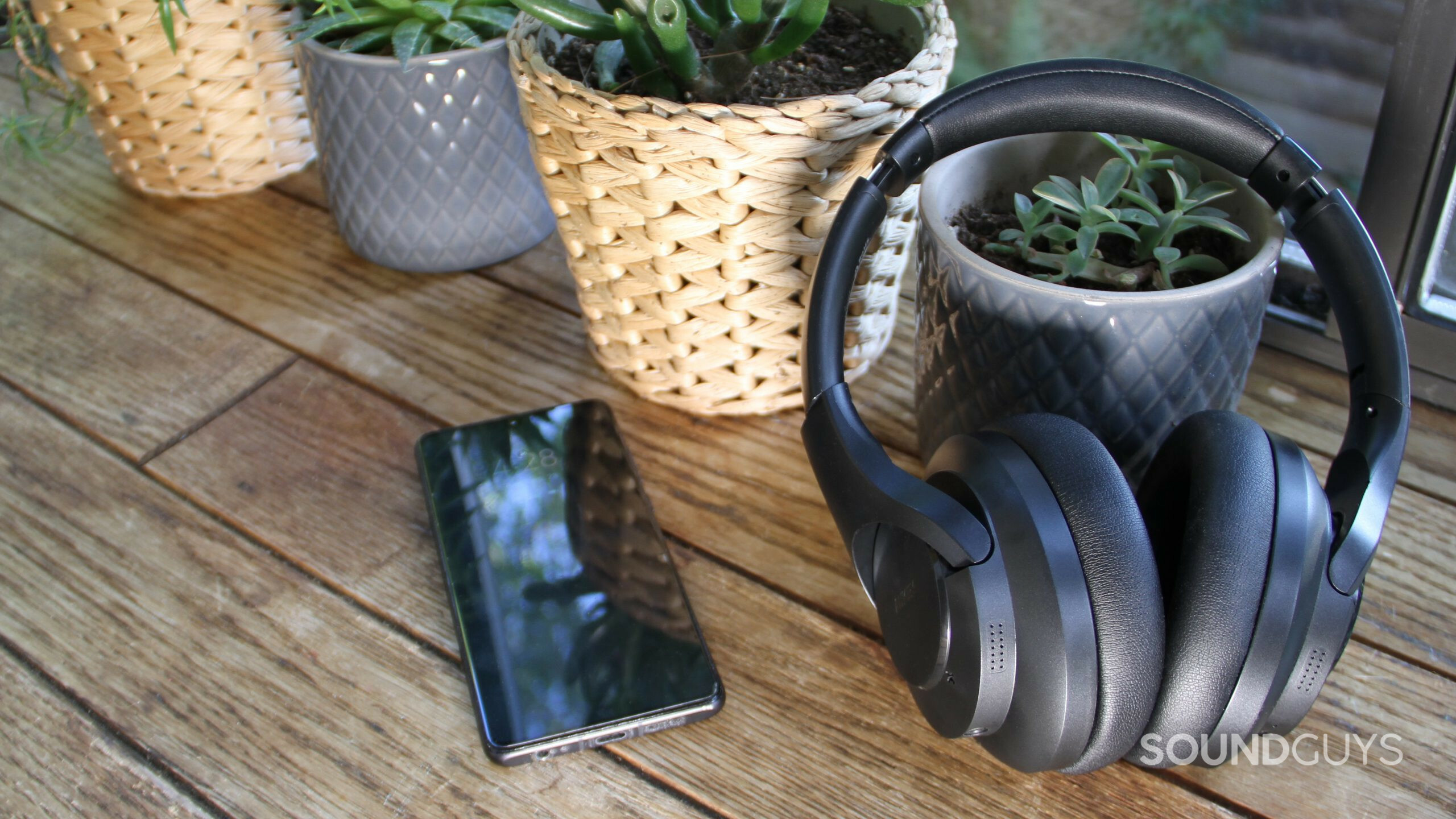 Leaning against a ceramic pot is the Aukey Hybrid Active Noise Canceling Headphones with a Huawei phone and a window in the background.
