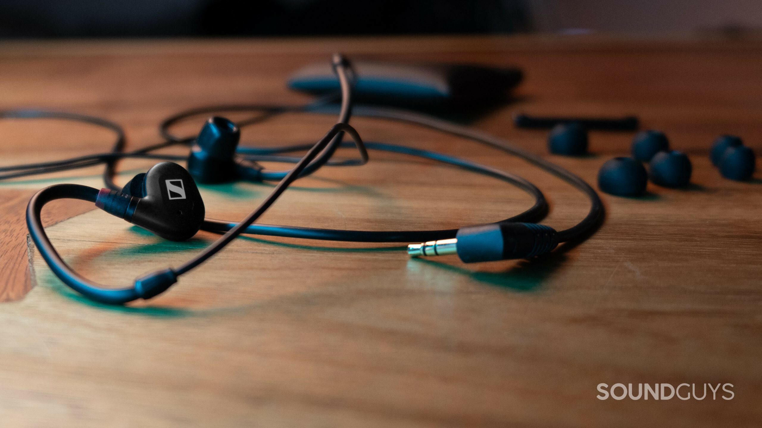 The wired cable plugged into the Sennheiser IE 100 PRO with ear tips and cloth bag, sitting on a wood surface.