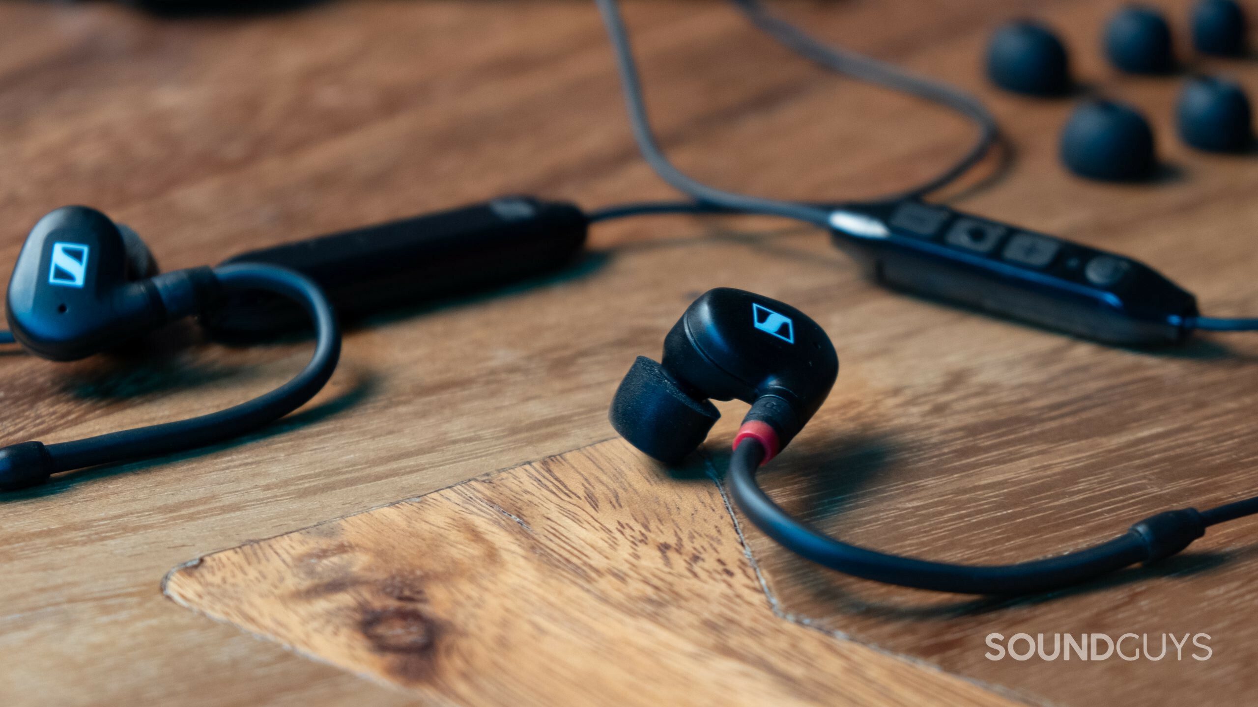 Close up of the Sennheiser IE 100 PRO Wireless with ear tips in the background on a wood table.