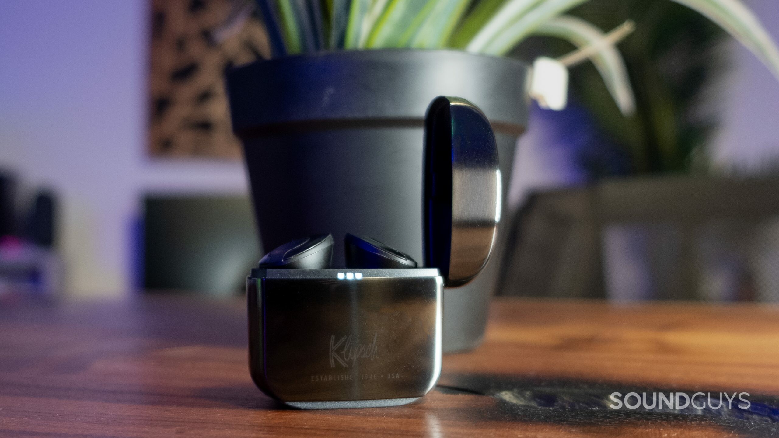 Klipsch T5 II ANC rests on a wood table with the case lid open and a potted plant in the background.