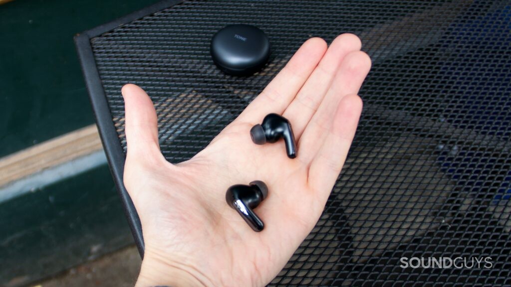 LG TONE Free FP8 earbuds resting in a hand with the case in the background on a metal table.
