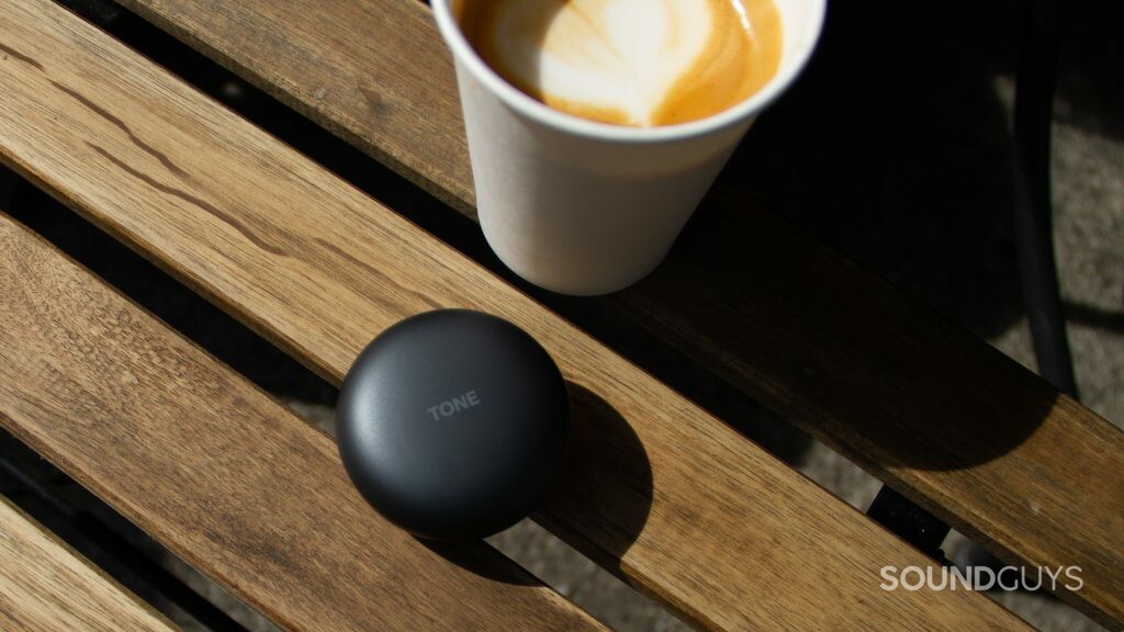 A close up of the LG TONE Free FP8 closed case next to a cortado coffee, sitting on a wood slat table.