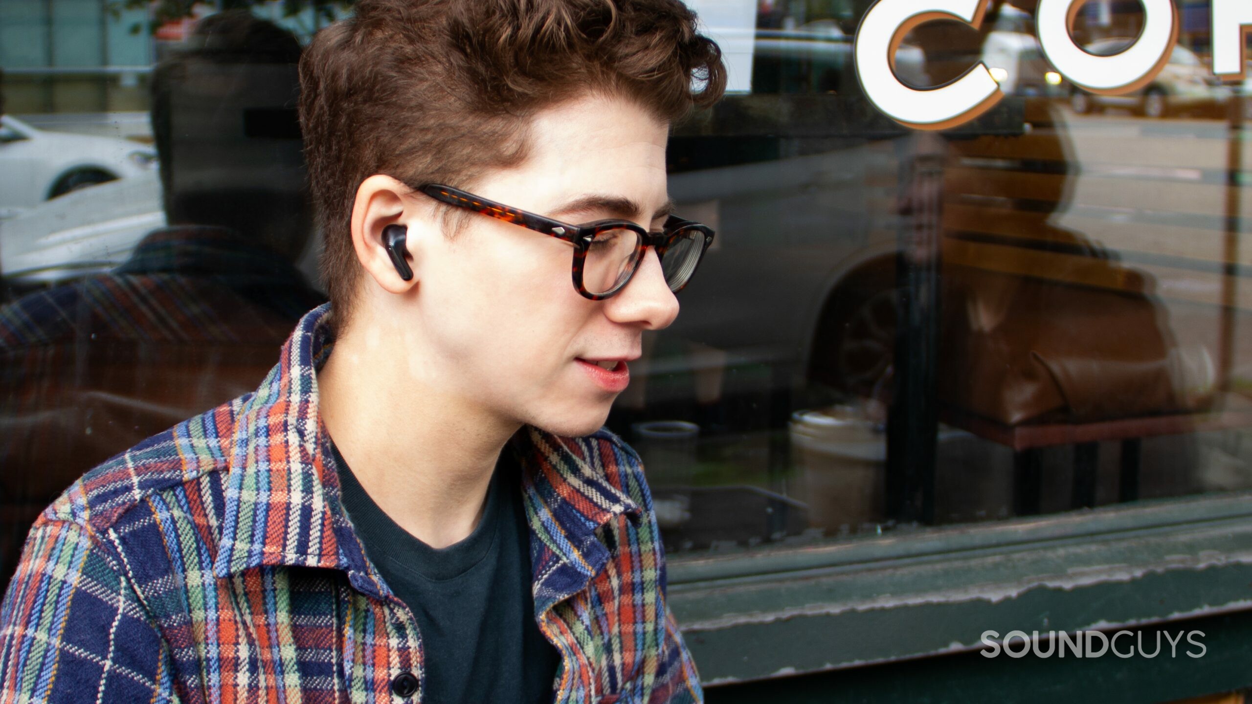 A man looking to the right and down wearing the LG TONE Free FP8 in front of a cafe window.