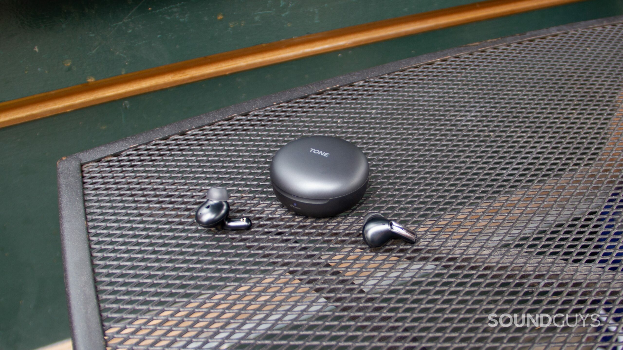 On a metal grate table the closed case and earbuds of the LG TONE Free FP8.