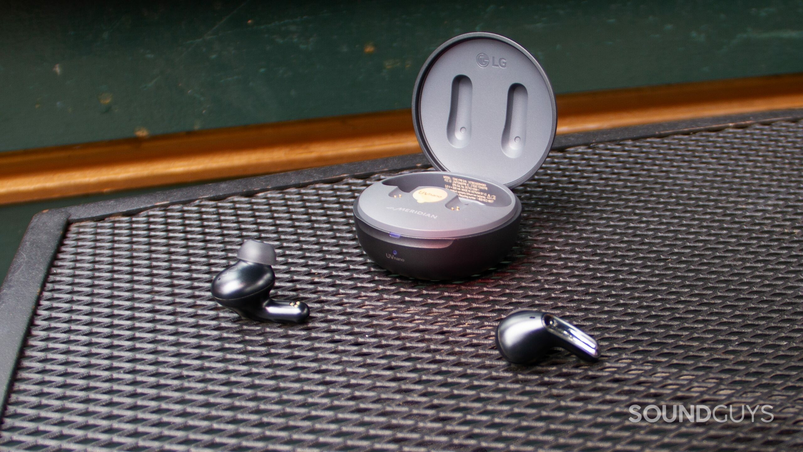 The open case of the LG TONE Free FP8 on a metal grated table outside with the buds placed on the table.