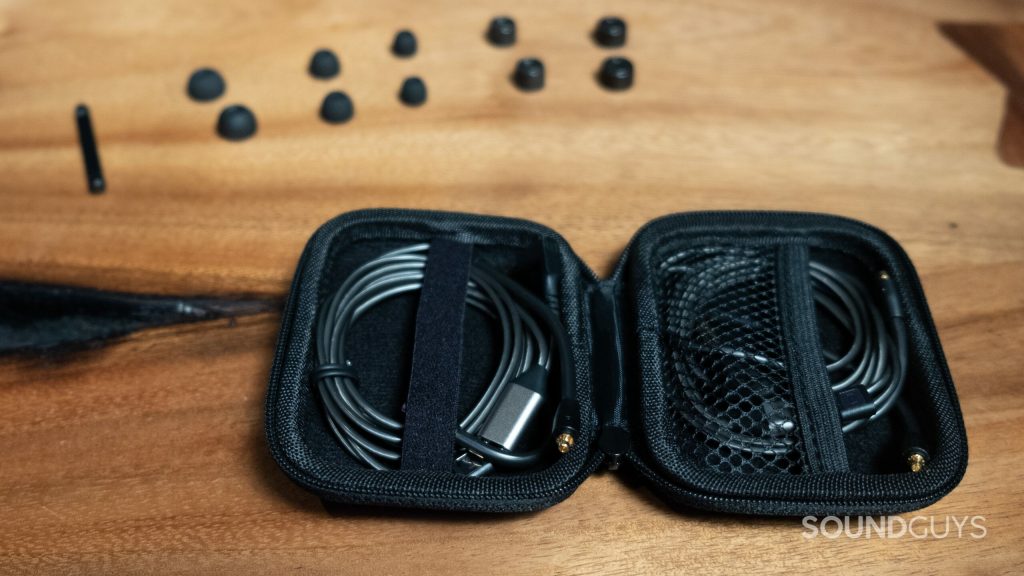The Sennheiser IE 900 open case with included detachable cables, different sized ear tips, and cleaning tool, all set on a wood surface.