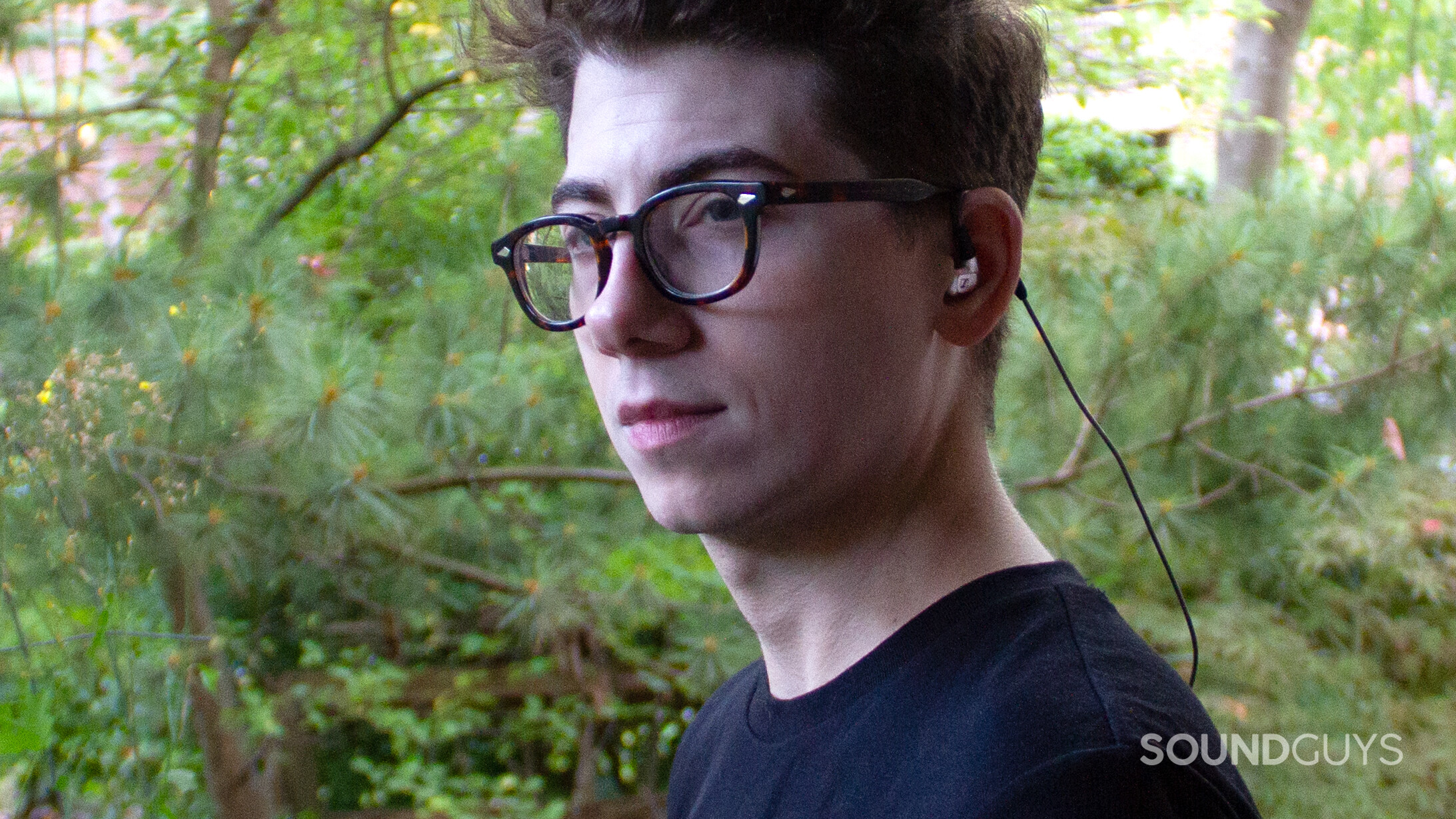 A man from the side wears the Sennheiser IE 900 earphones outside in front of greenery.