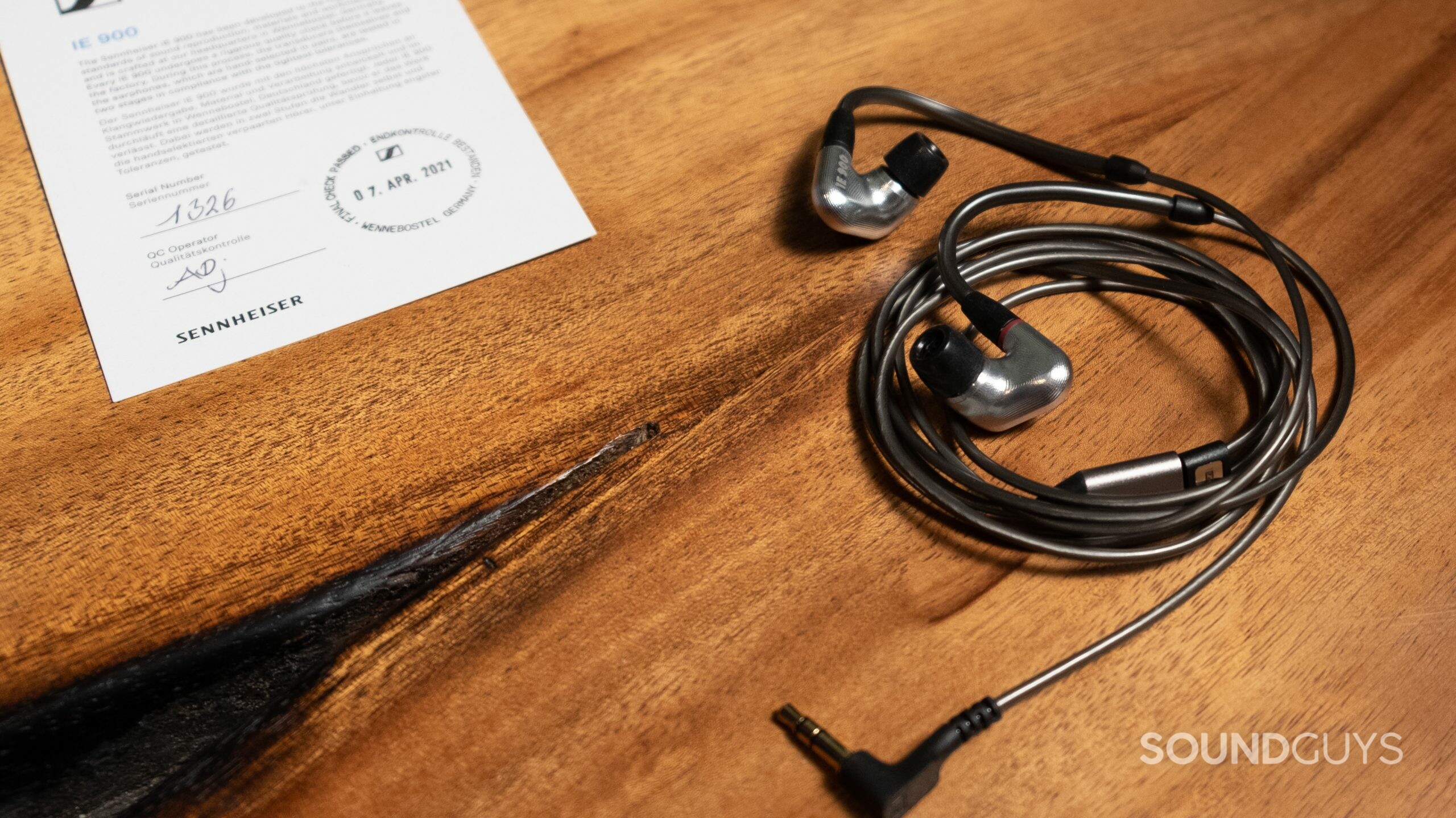 The Sennheiser IE 900 earphones coiled on a wood surface with accompanying Certificate of Authenticity.