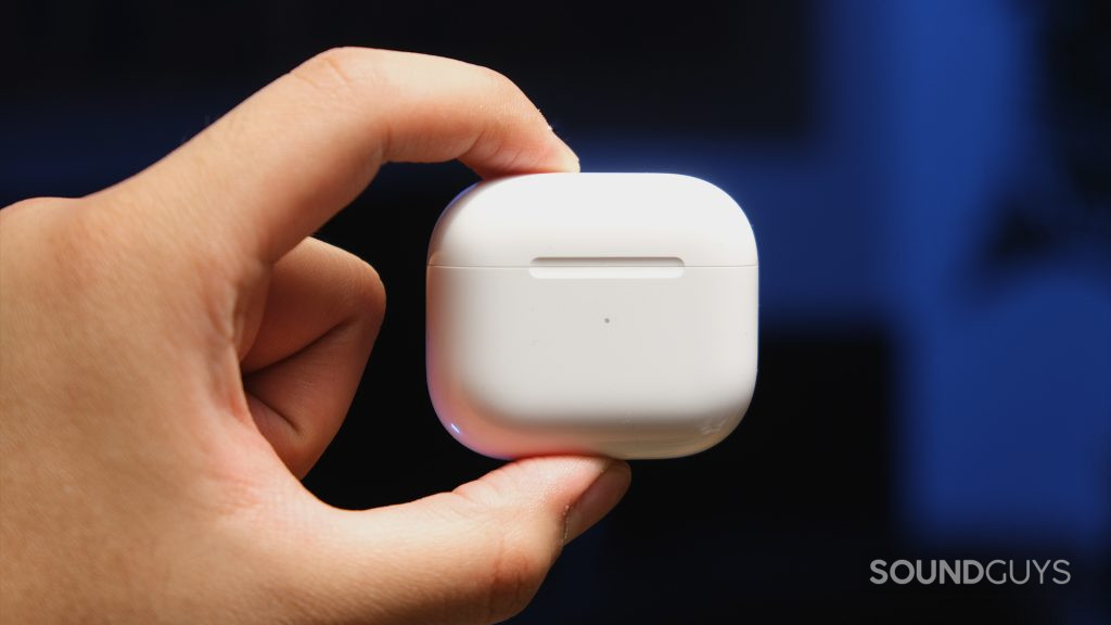 A hand pinches the Apple AirPods (3rd generation) charging case to display its plain white exterior and minimalist indentation.