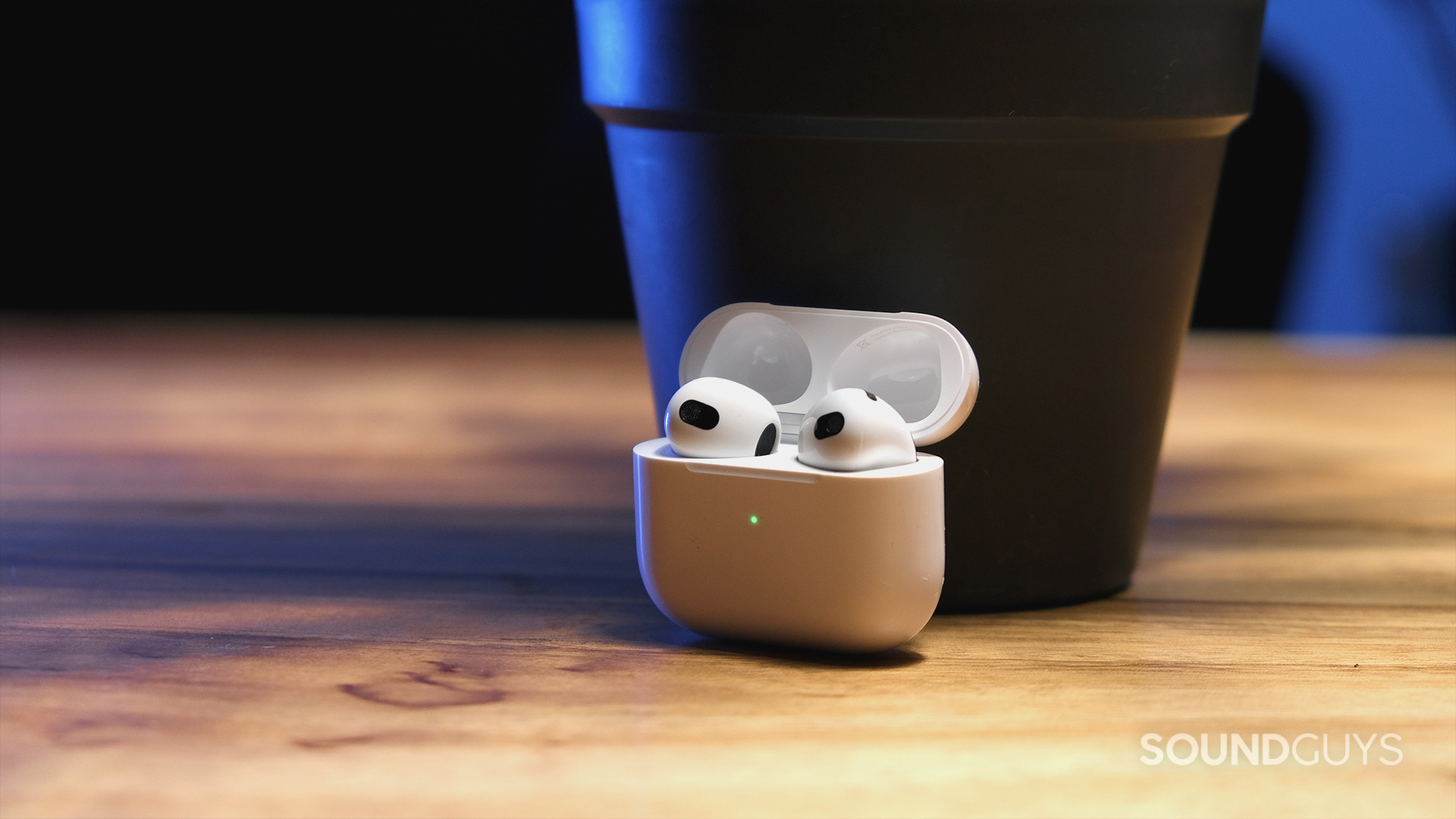 The Apple AirPods (3rd generation) open case holds the earbuds and sits on a wood surface.